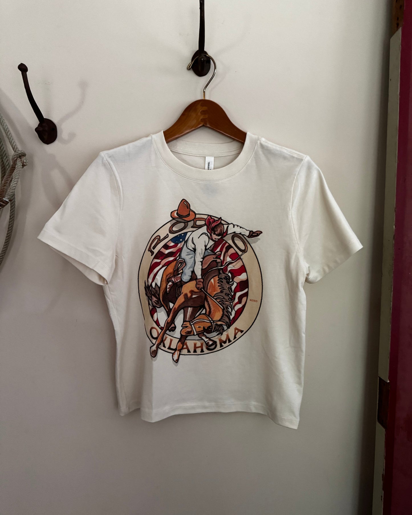 White t-shirt with a graphic design of a horse and text, hanging on a wooden hanger against a white wall.