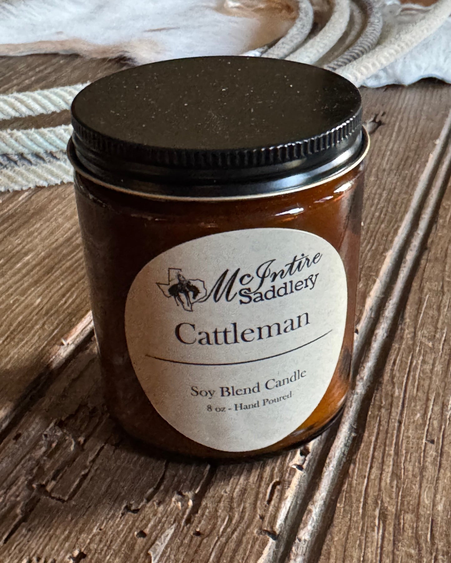 Jar candle labeled 'The Cattleman' on a wooden surface