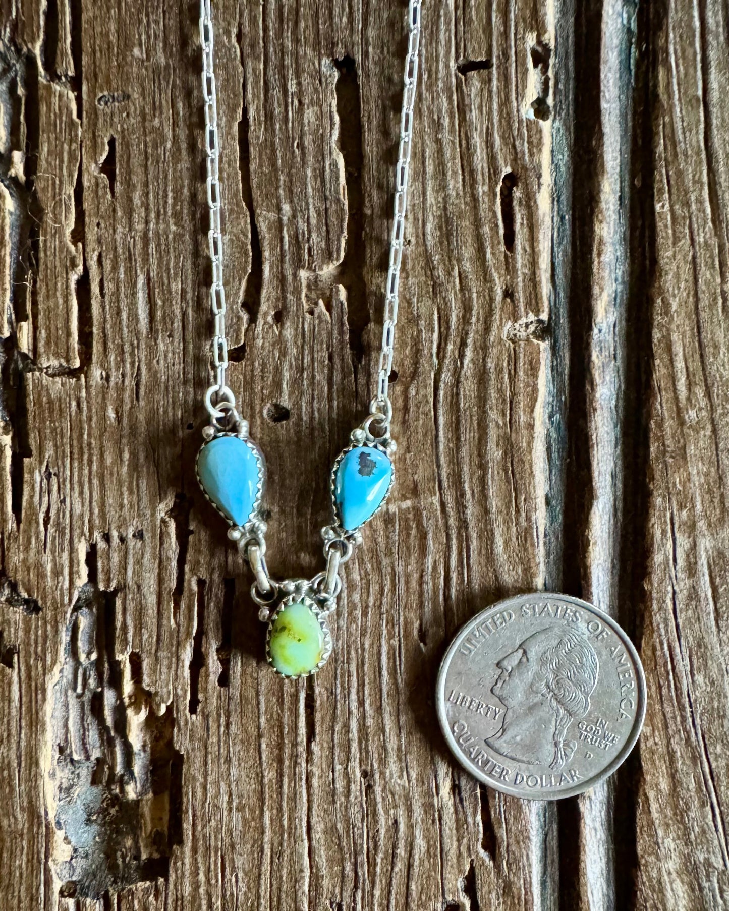 Necklace with turquoise and green beads on a wooden surface next to a quarter for scale.