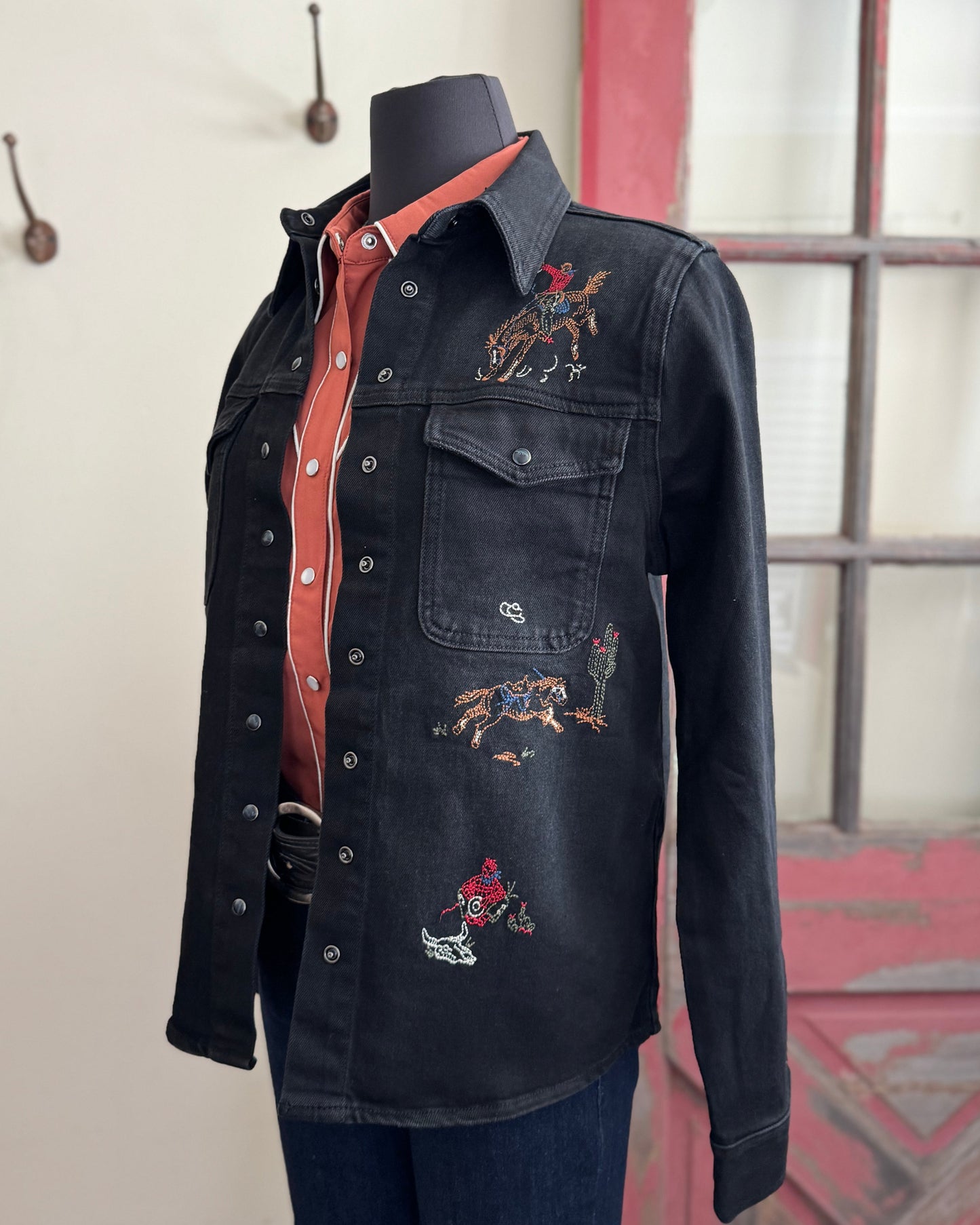 Black denim shirt with embroidered designs on a mannequin against a neutral background.