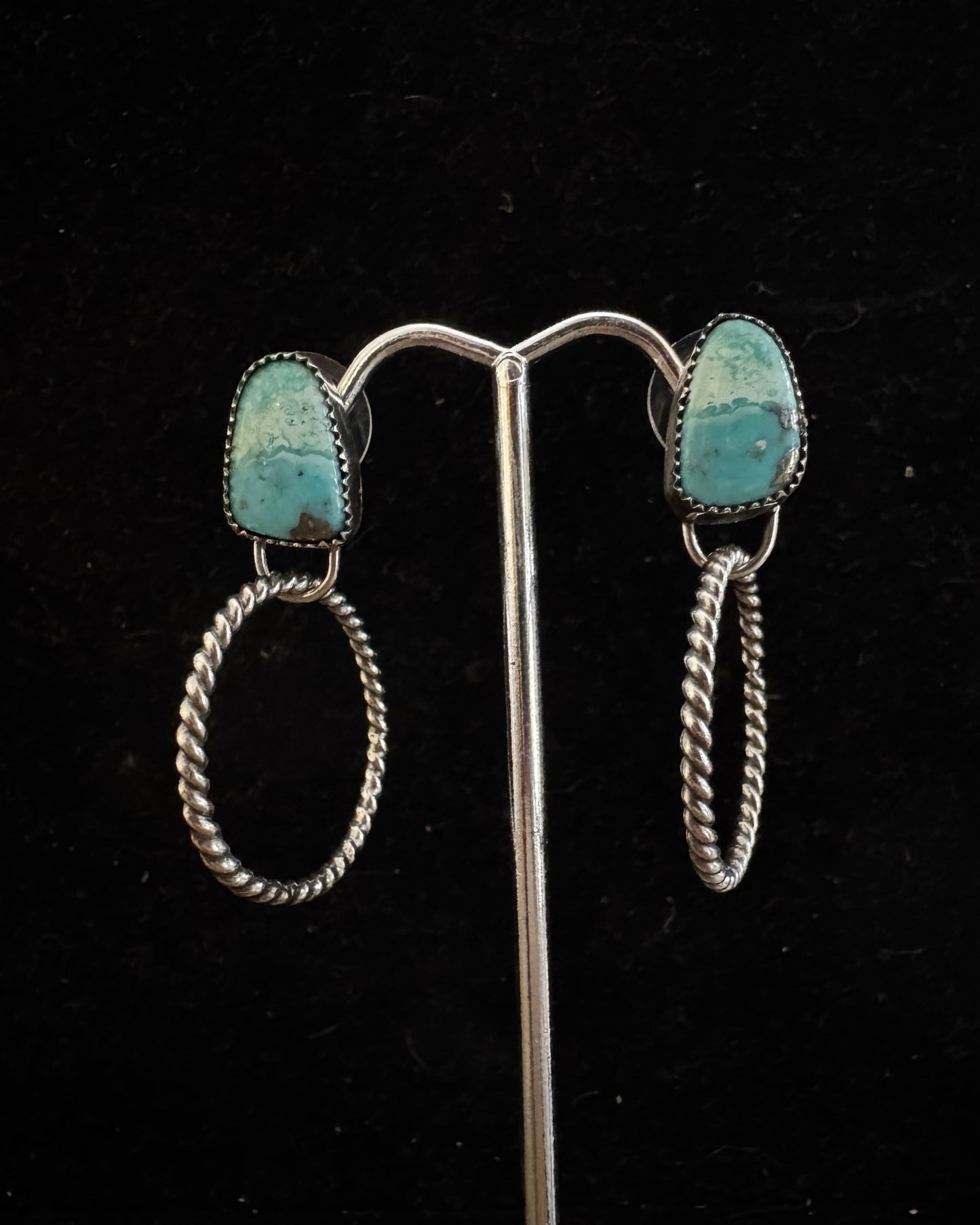 Pair of silver earrings with turquoise stones on a black background