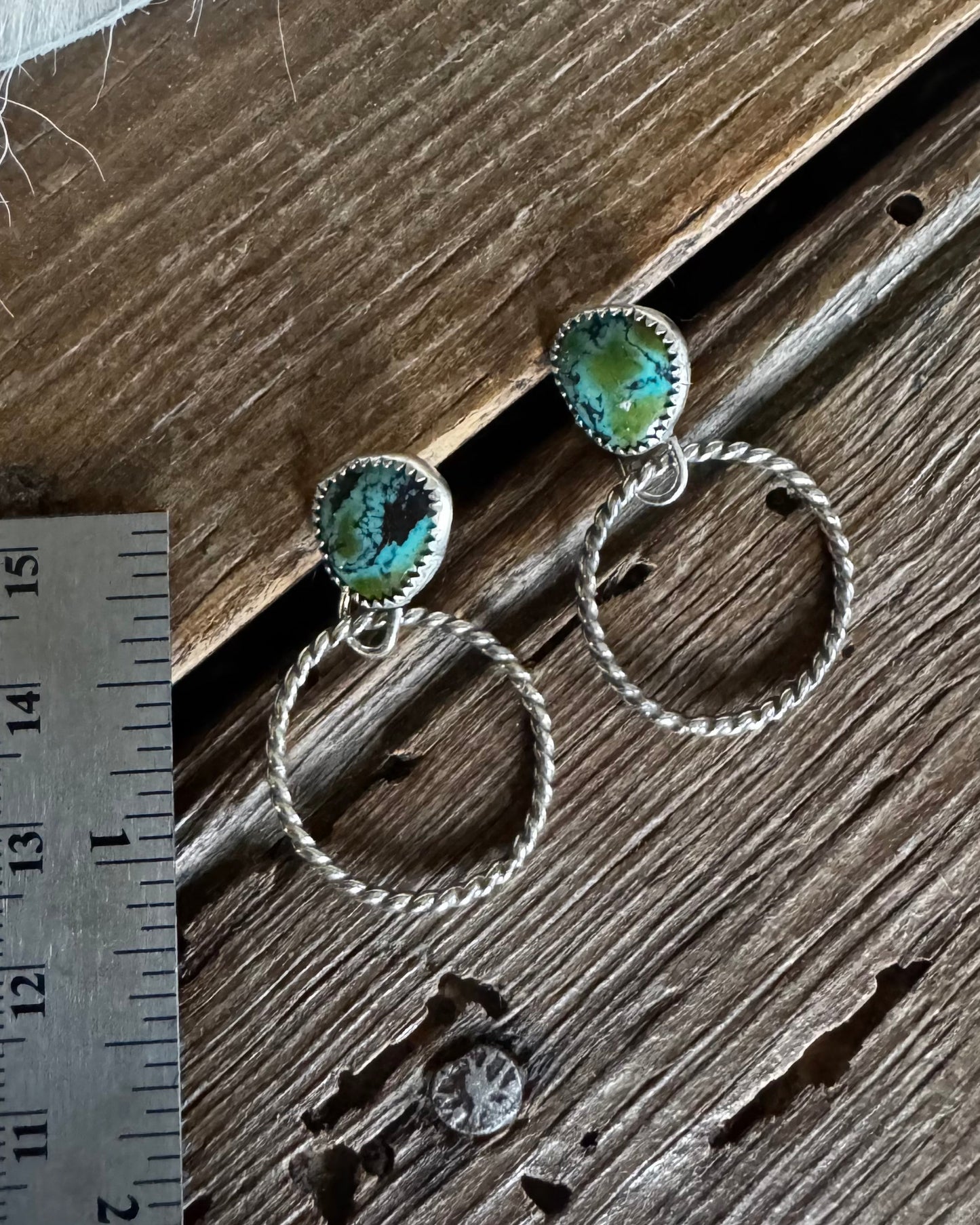 Silver hoop earrings with turquoise stones on a wooden surface next to a ruler.