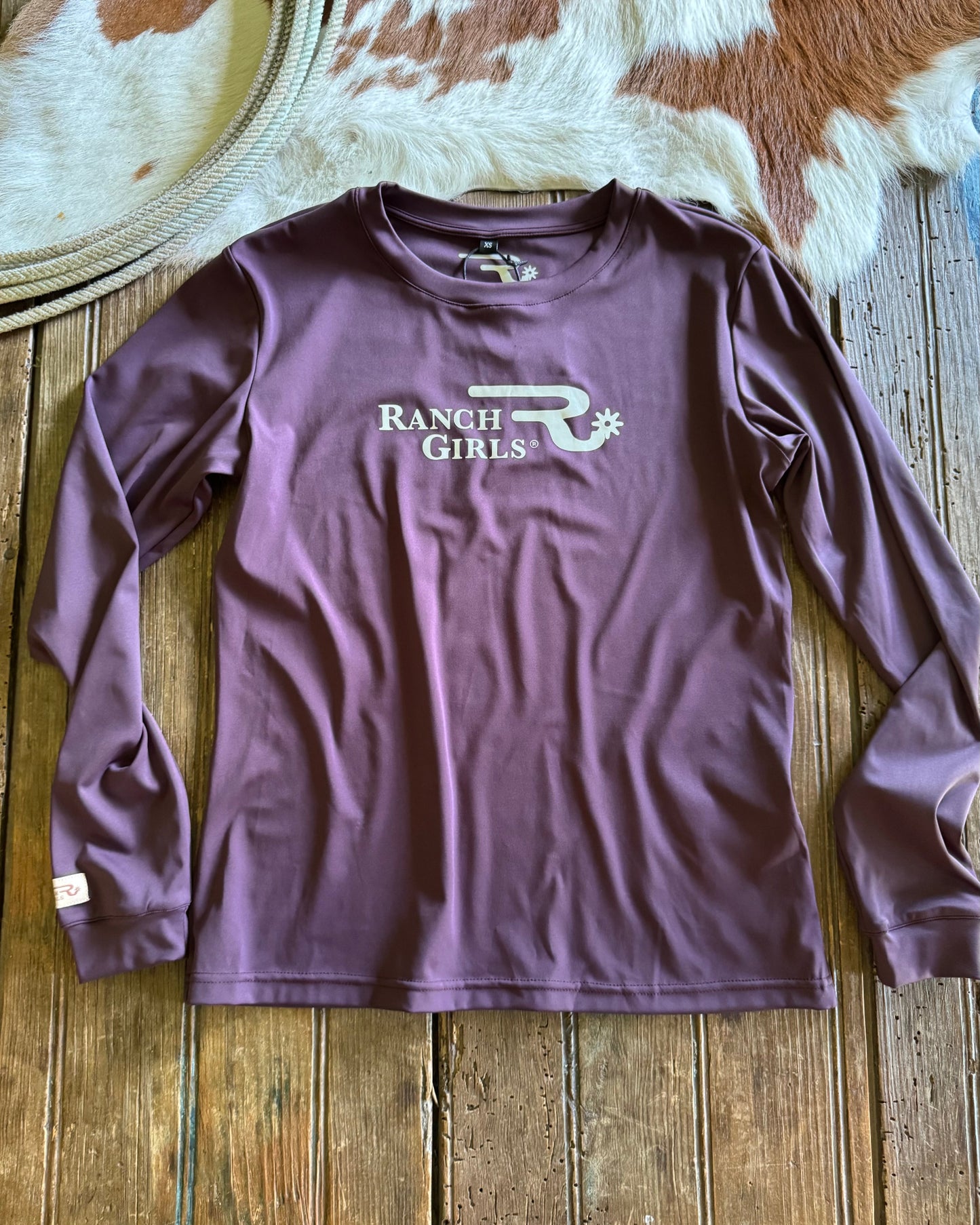 Purple long-sleeve shirt with 'Ranch Girls' logo on a wooden surface