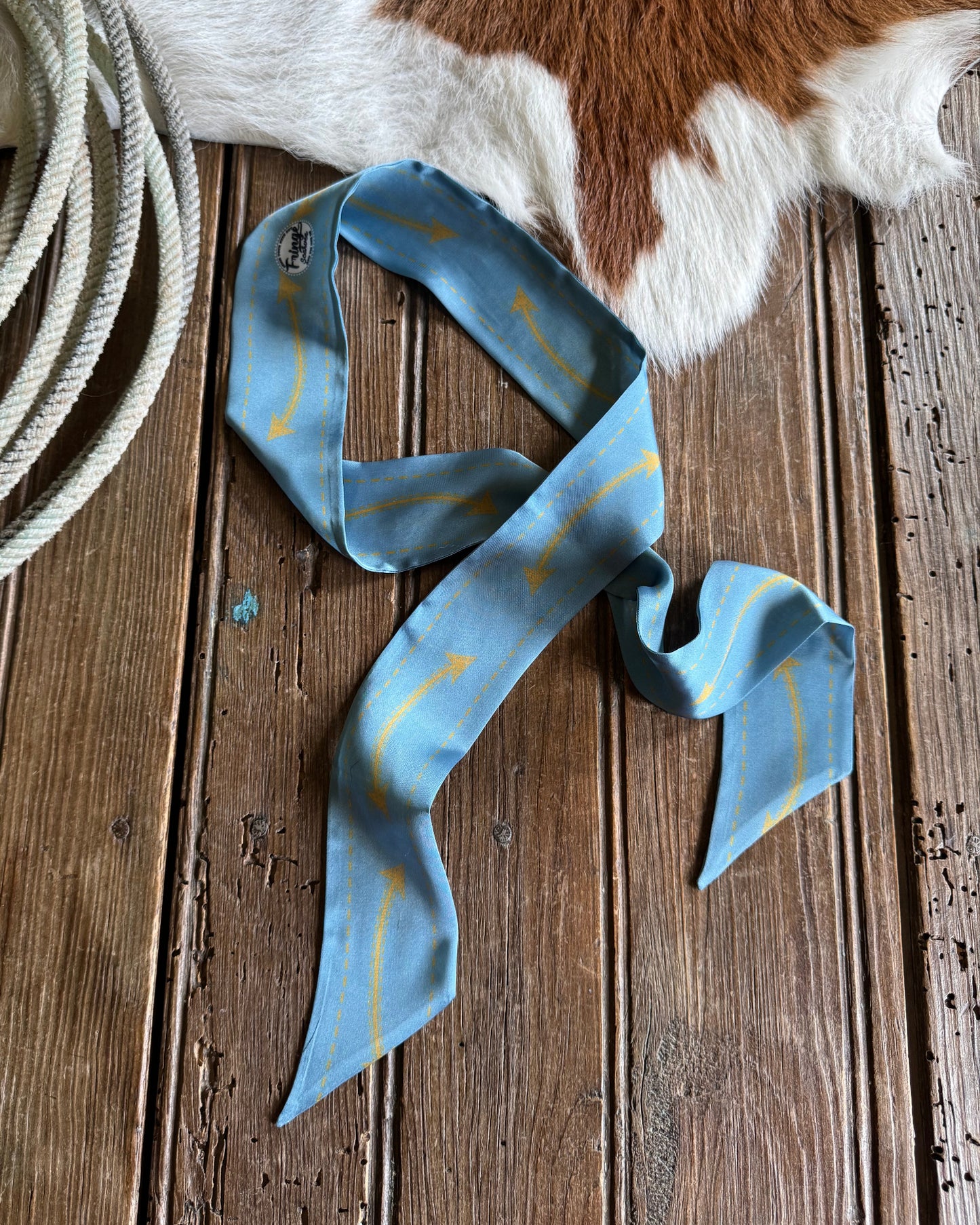 Blue ribbon scarf with gold accents on a wooden surface next to a cowhide rug.
