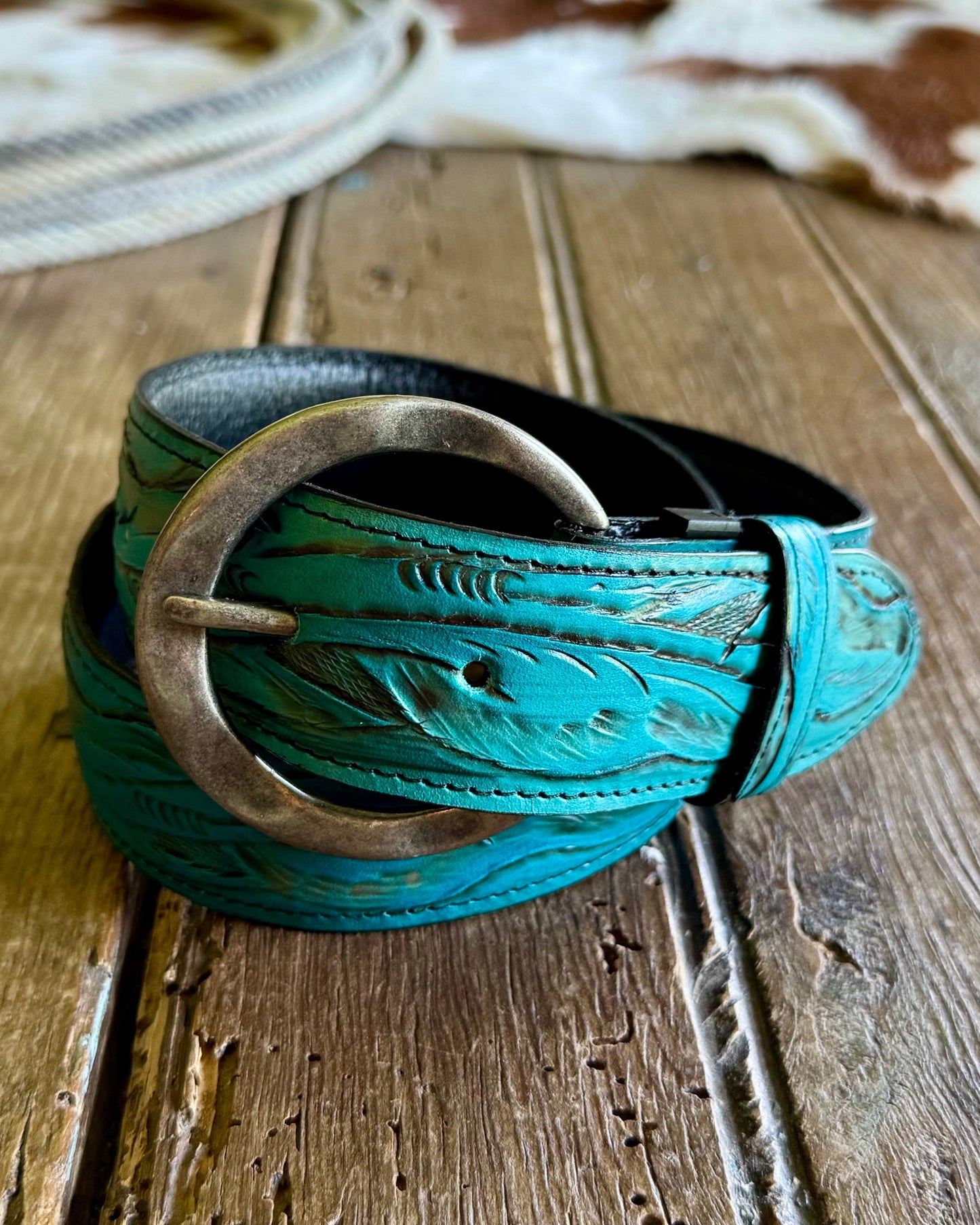 Turquoise leather belt with metal buckle on a wooden surface