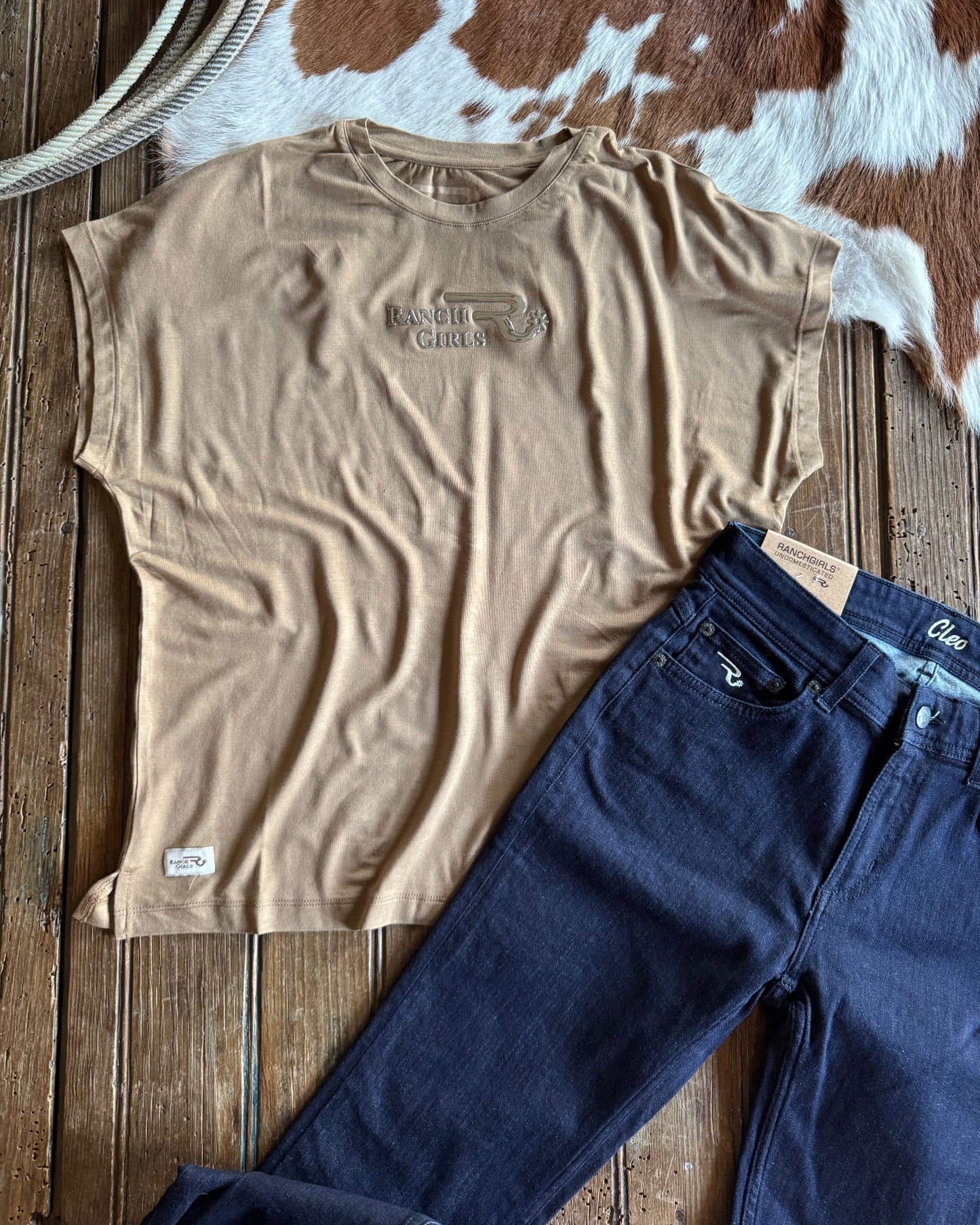 Beige t-shirt and blue jeans on a wooden surface with cowhide rug