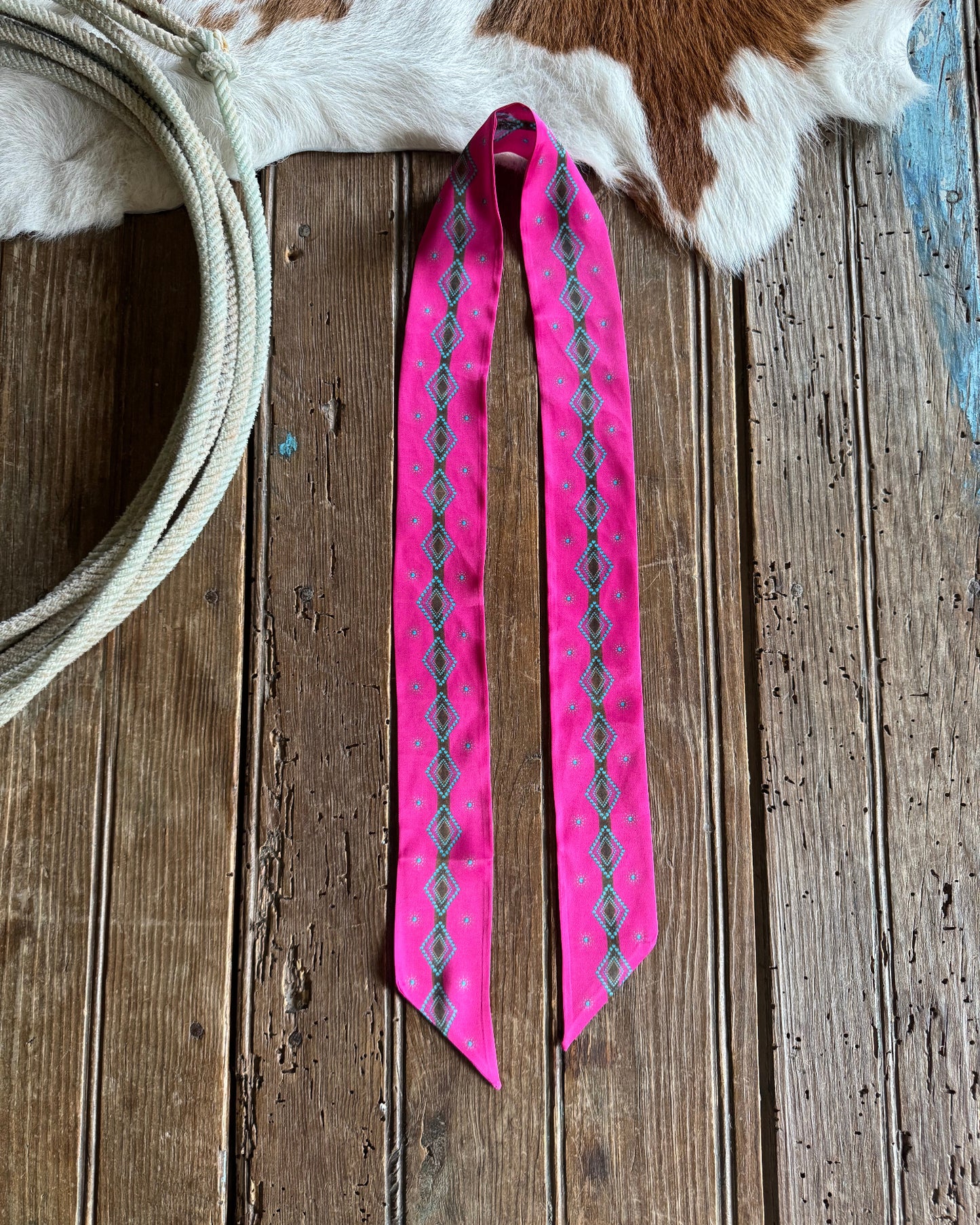 pink ribbon scarf with a pattern on a wooden surface next to a cowhide and rope.