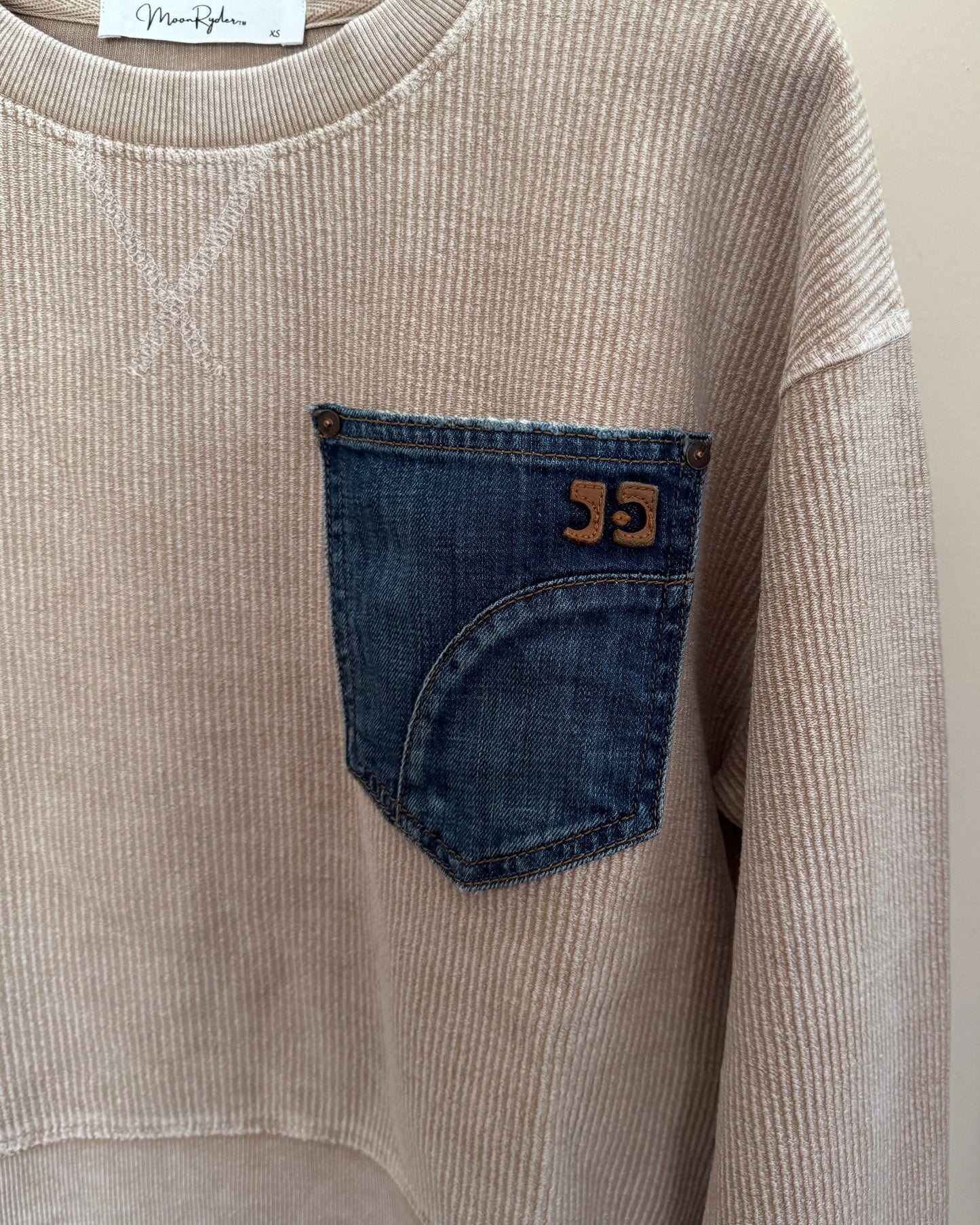 Beige corduroy shirt with a blue pocket and brand label on a light background