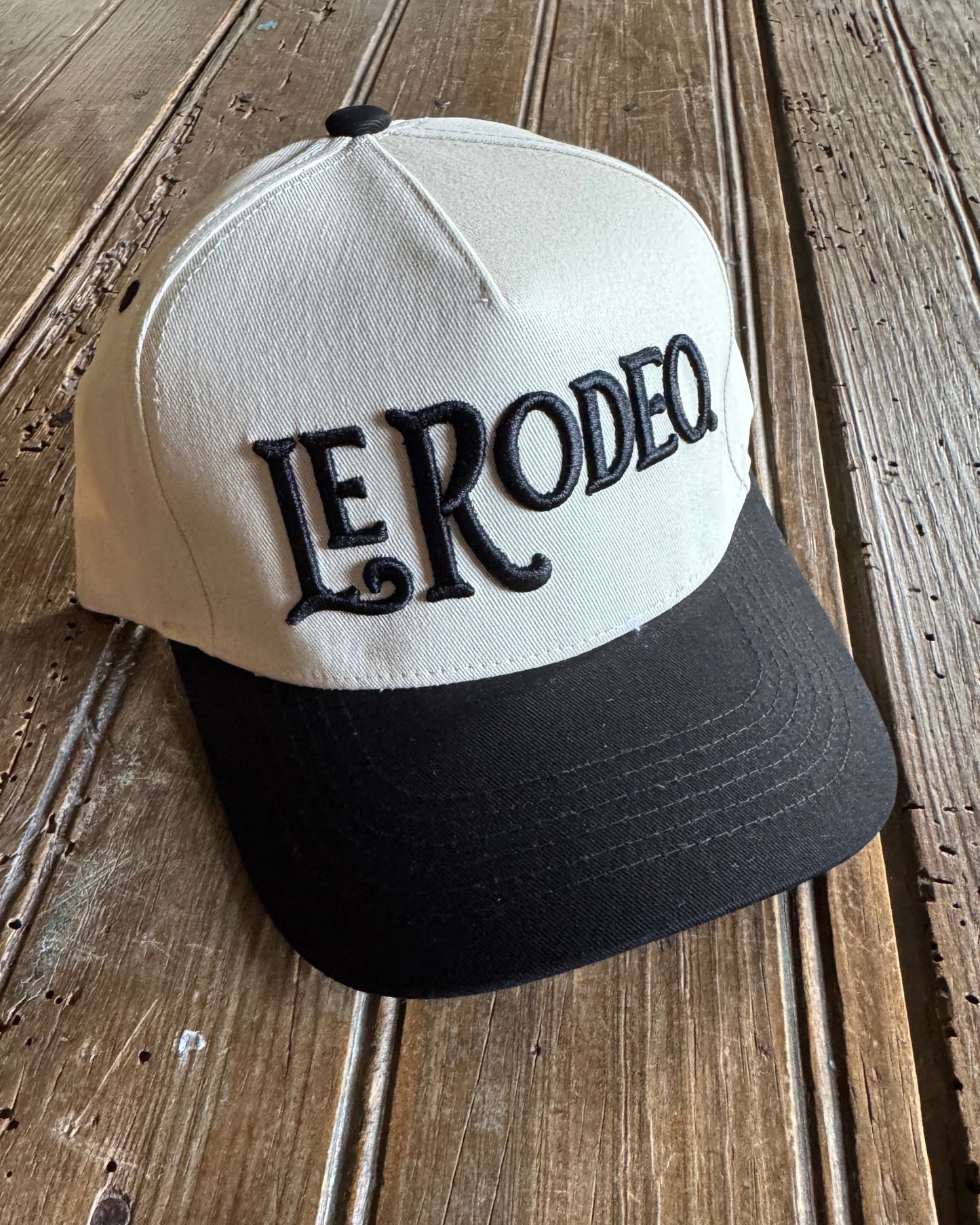 Black and cream hat with 'Le Rodeo' branding, on a wooden surface.