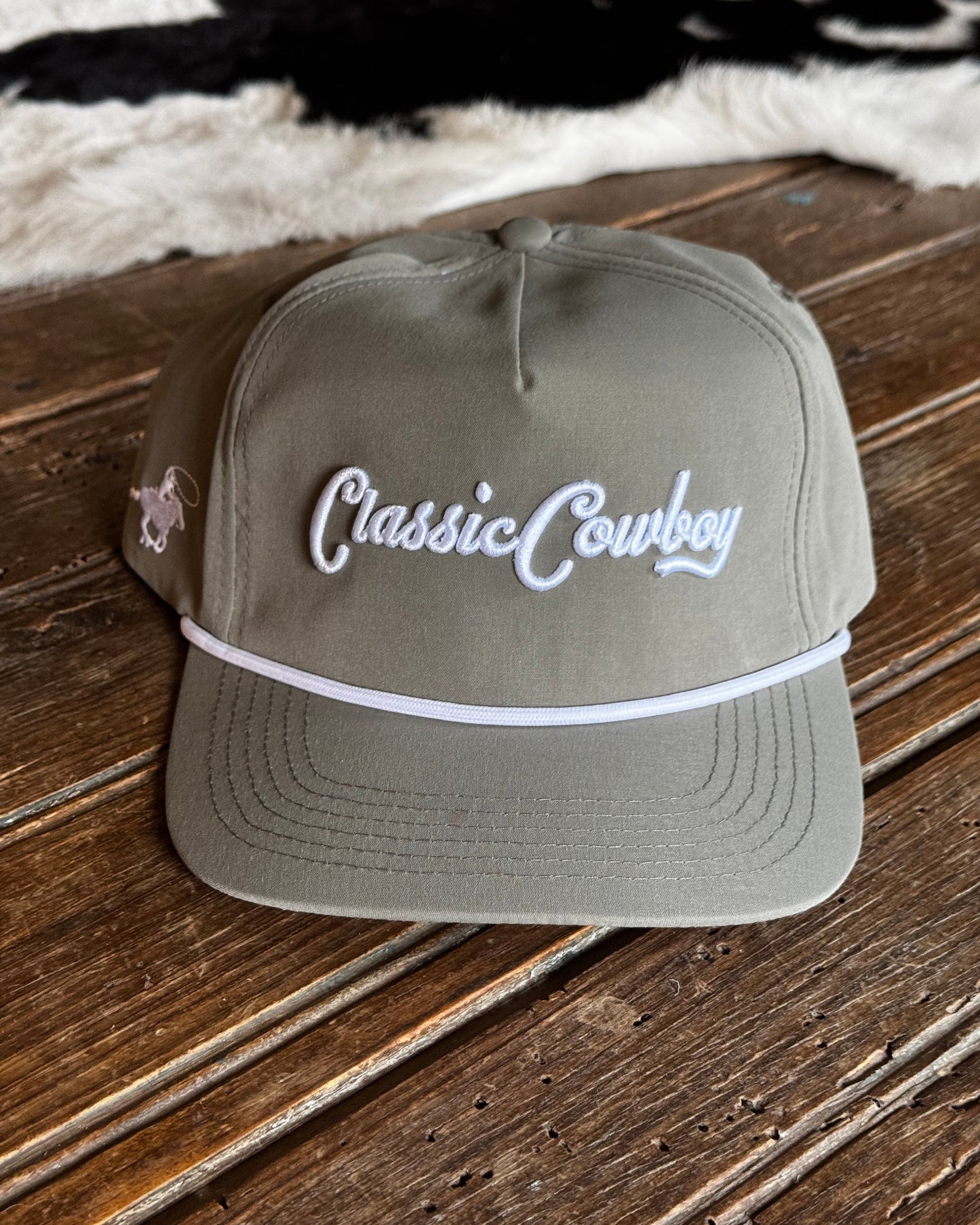 Green cap with 'Classic Cowboy' text on a wooden surface with cowhide rug in the background