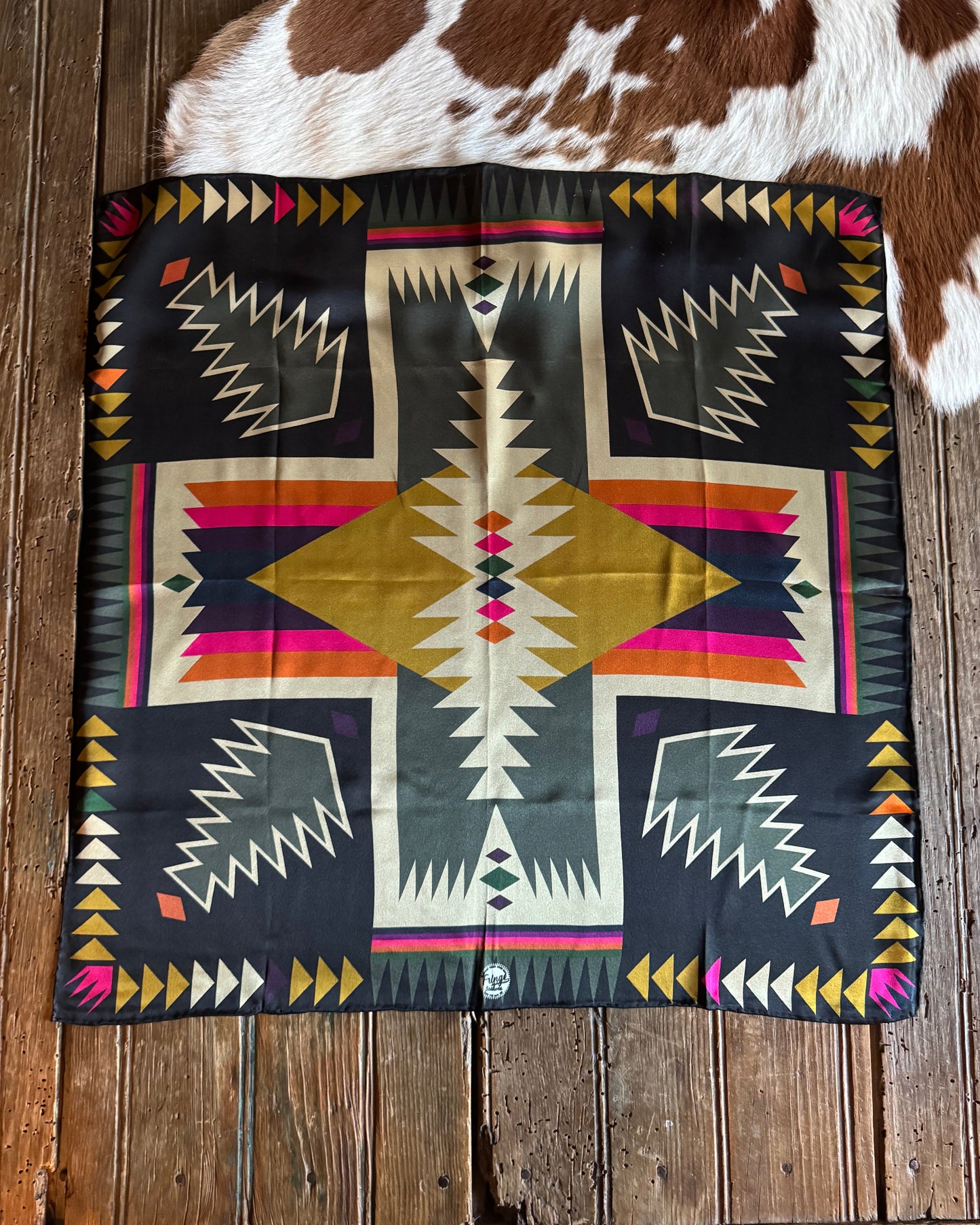 Colorful patterned scarf on a wooden surface with cowhide rug and hat in the background