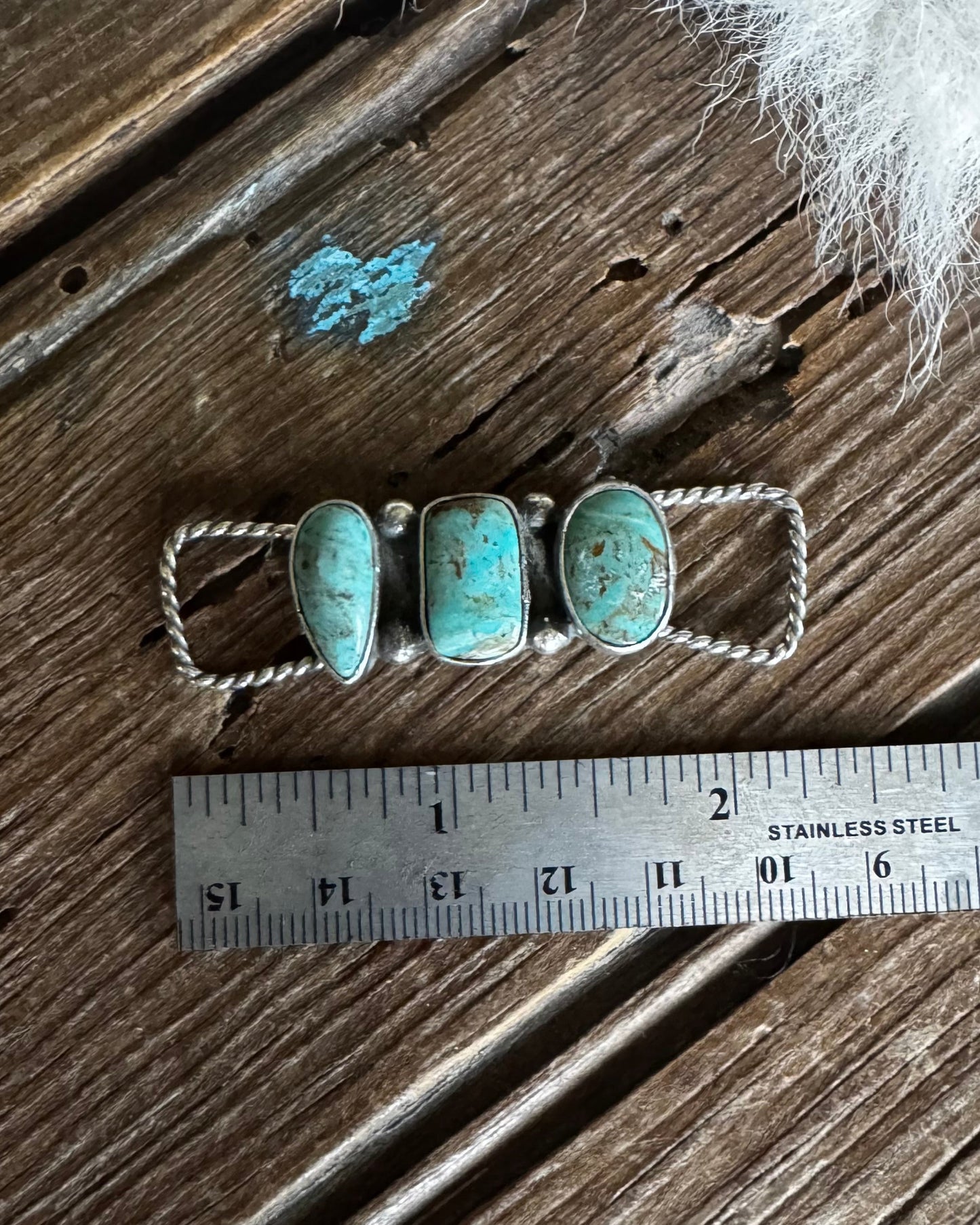 Silver ring with turquoise stones on a wooden surface with a ruler for scale.