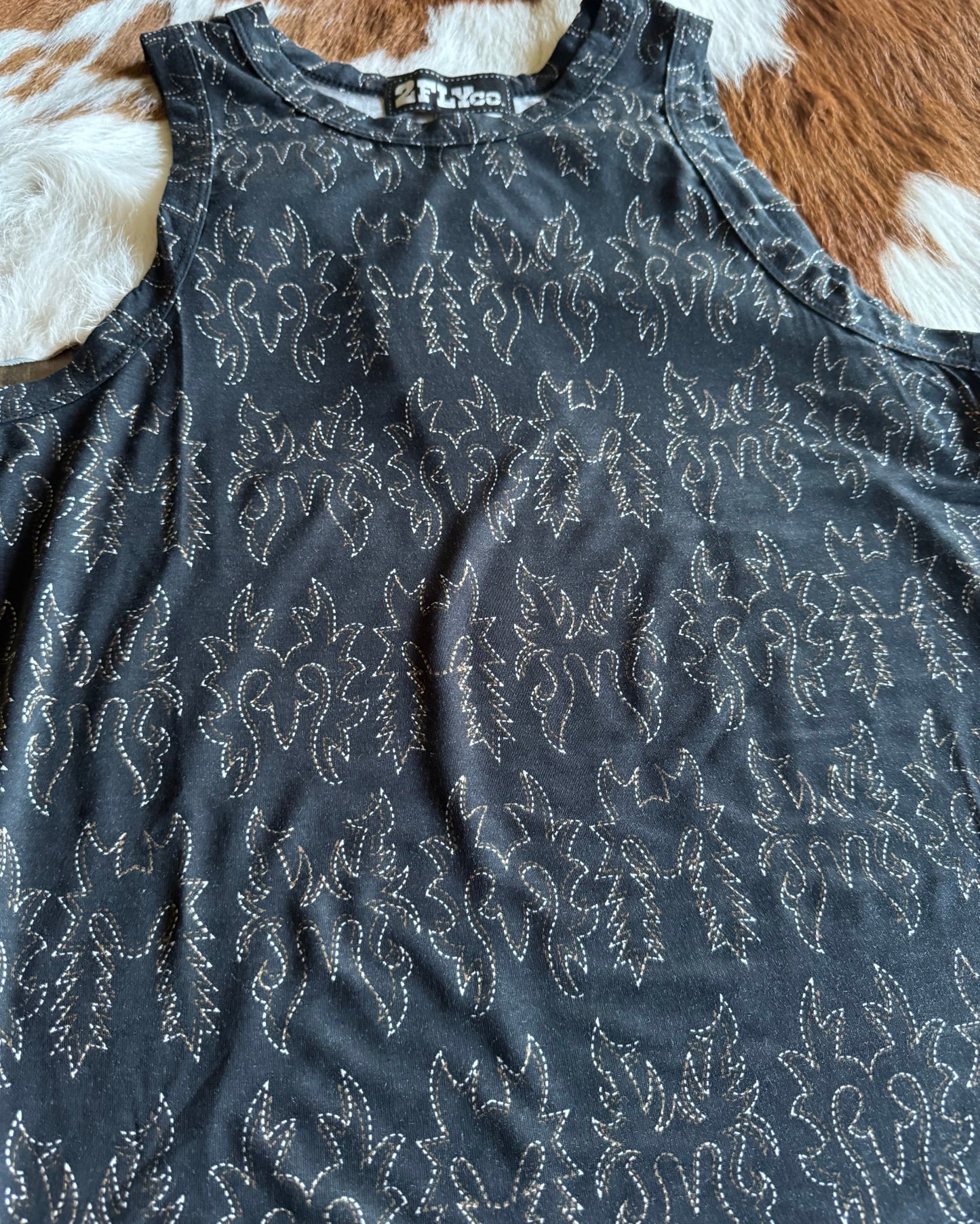 black tank top with white boot stitch pattern on a brown and white cowhide rug