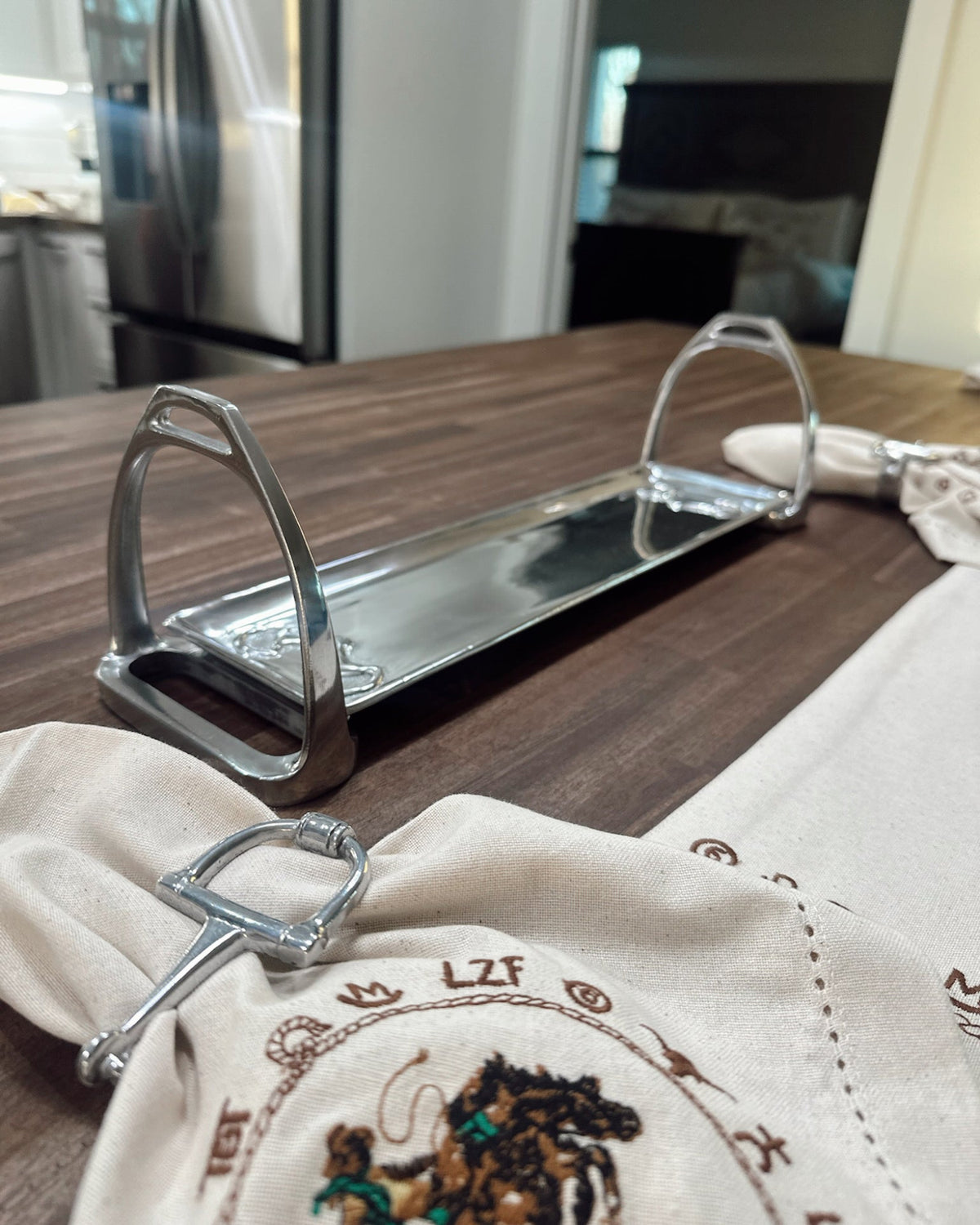 Metal equestrian stirrup napkin holder on a wooden table with embroidered napkins.
