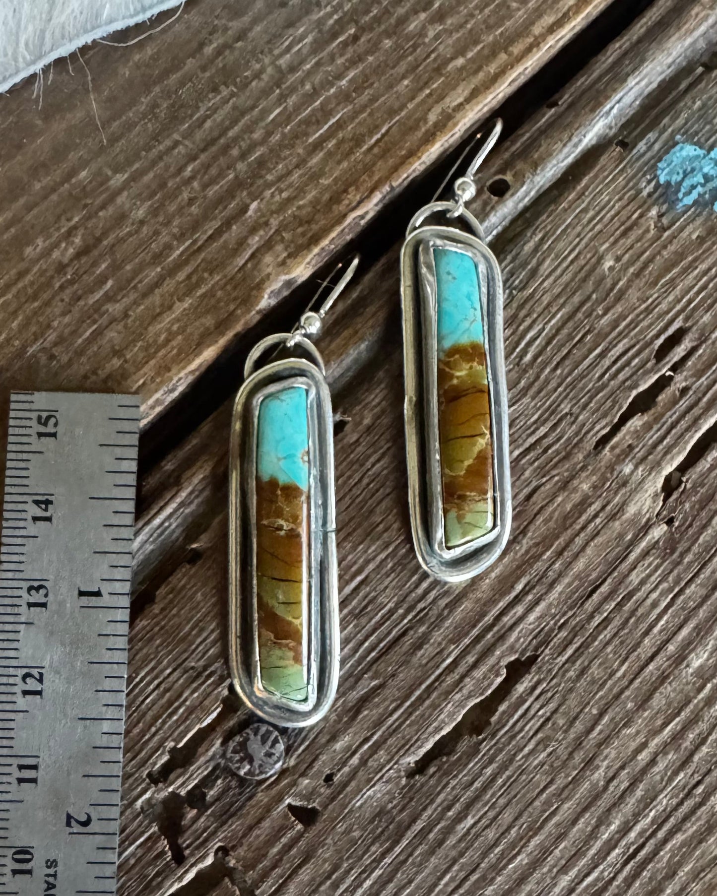 Pair of earrings with turquoise and amber stones on a wooden surface with a ruler for scale.
