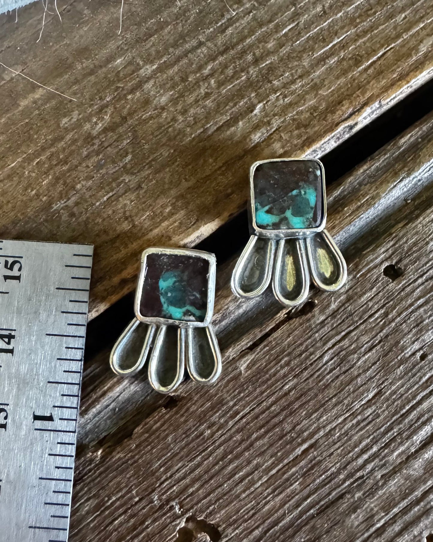 Pair of earrings on a wooden surface with a ruler for scale.
