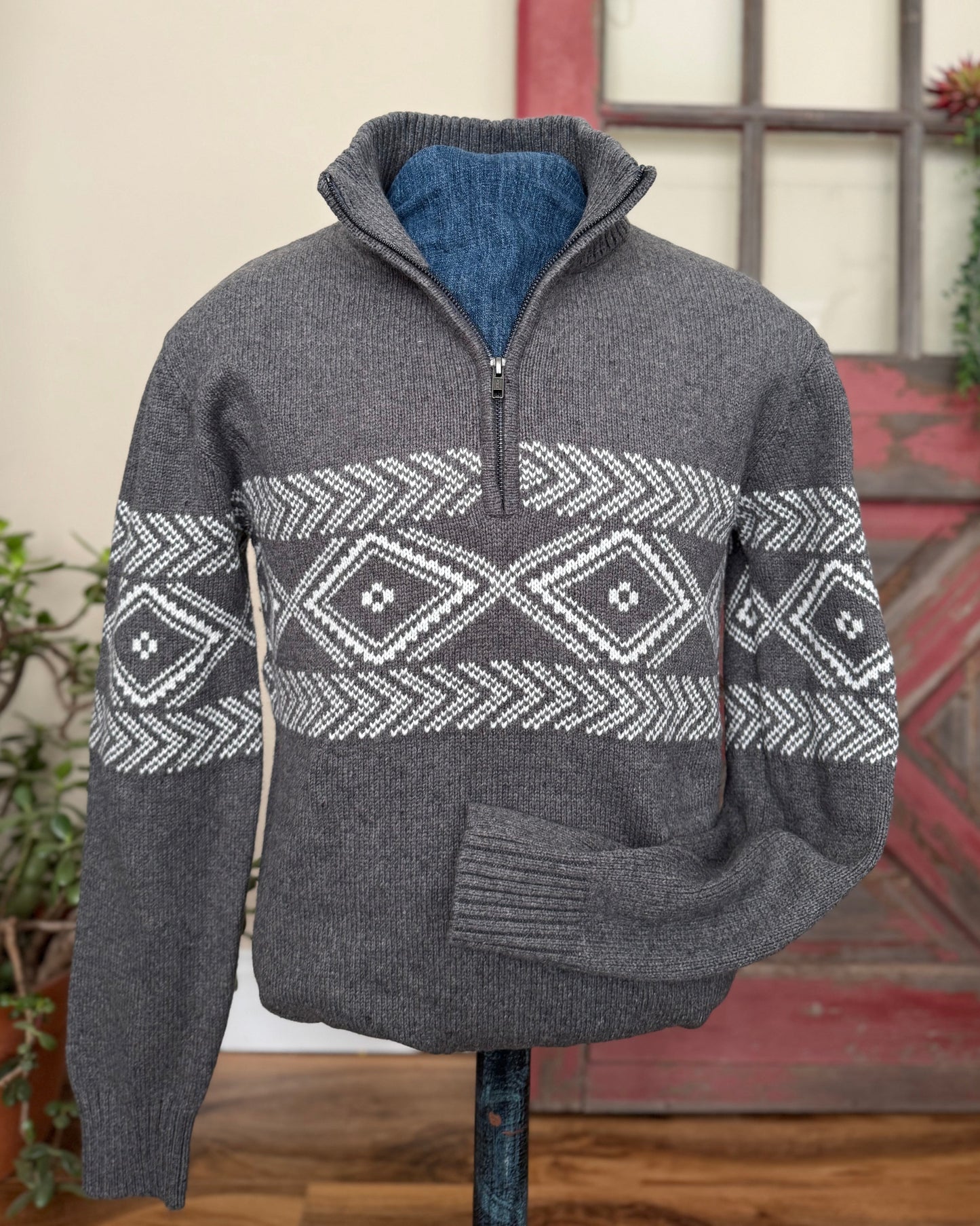 Gray sweater with a patterned design on a mannequin against a rustic background