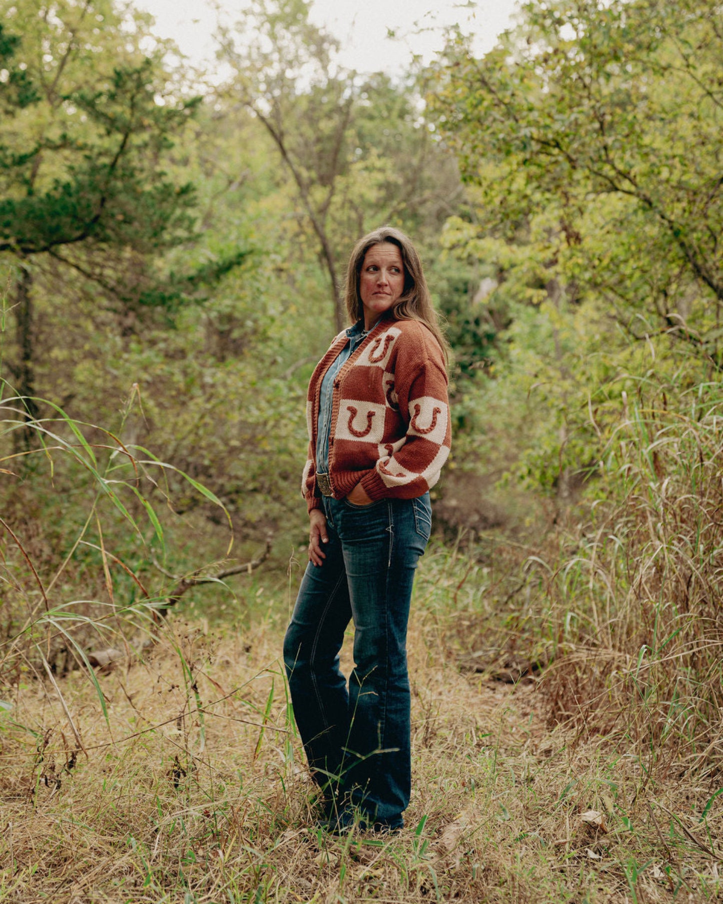 Woman wearing a patterned sweater and jeans standing in a forest