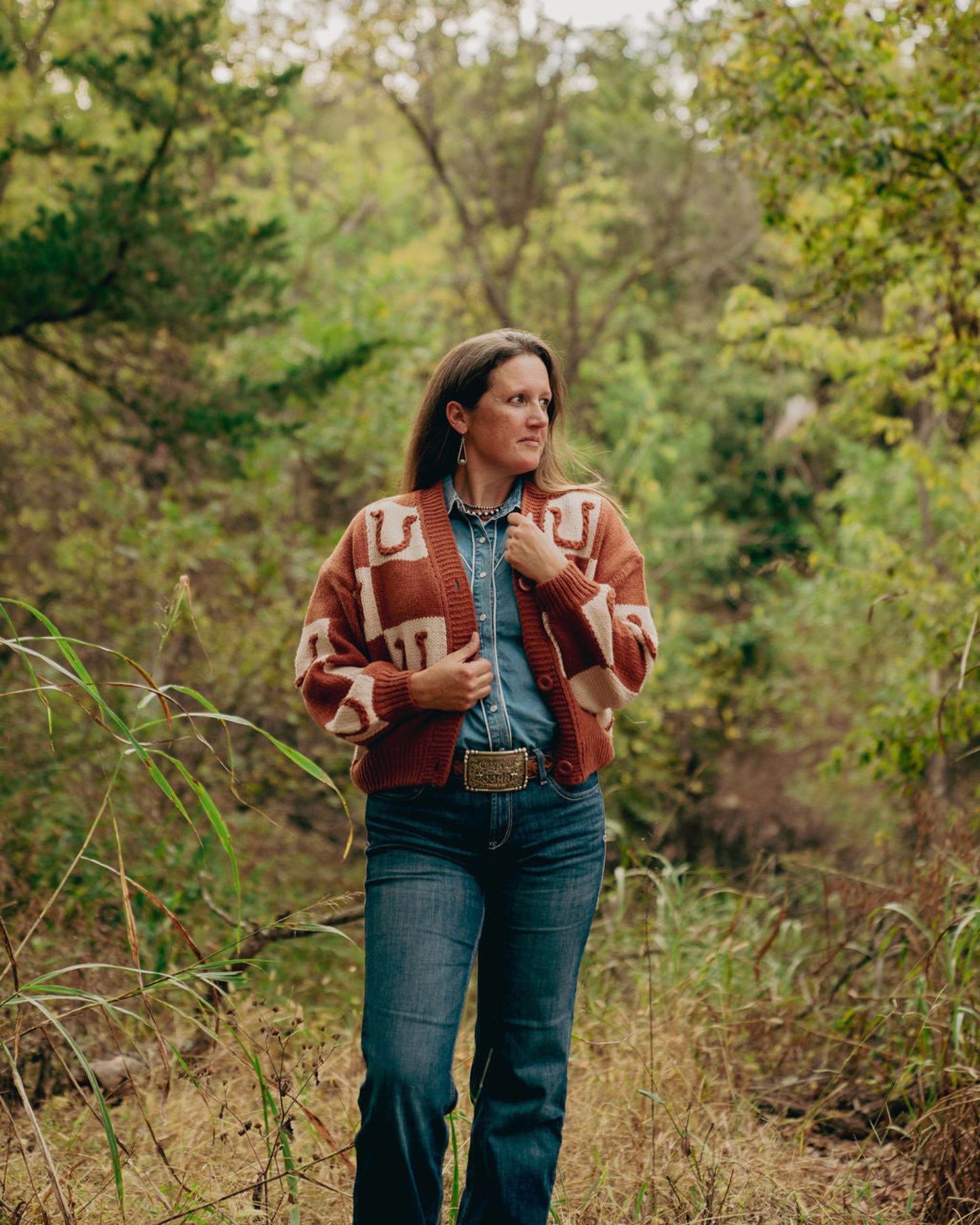 Woman wearing a patterned jacket and jeans standing in a forest