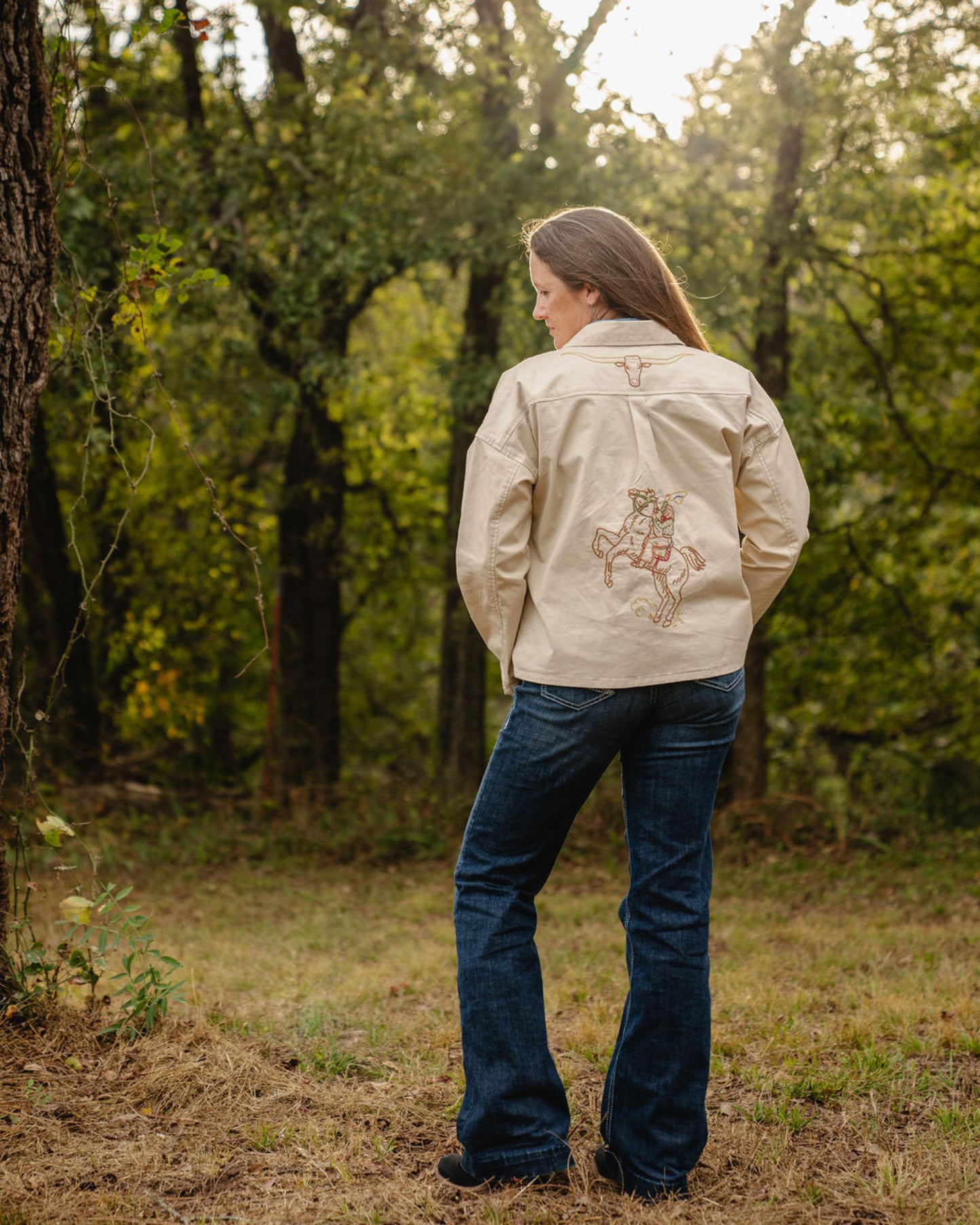 Person wearing a beige jacket with a design in a forest setting