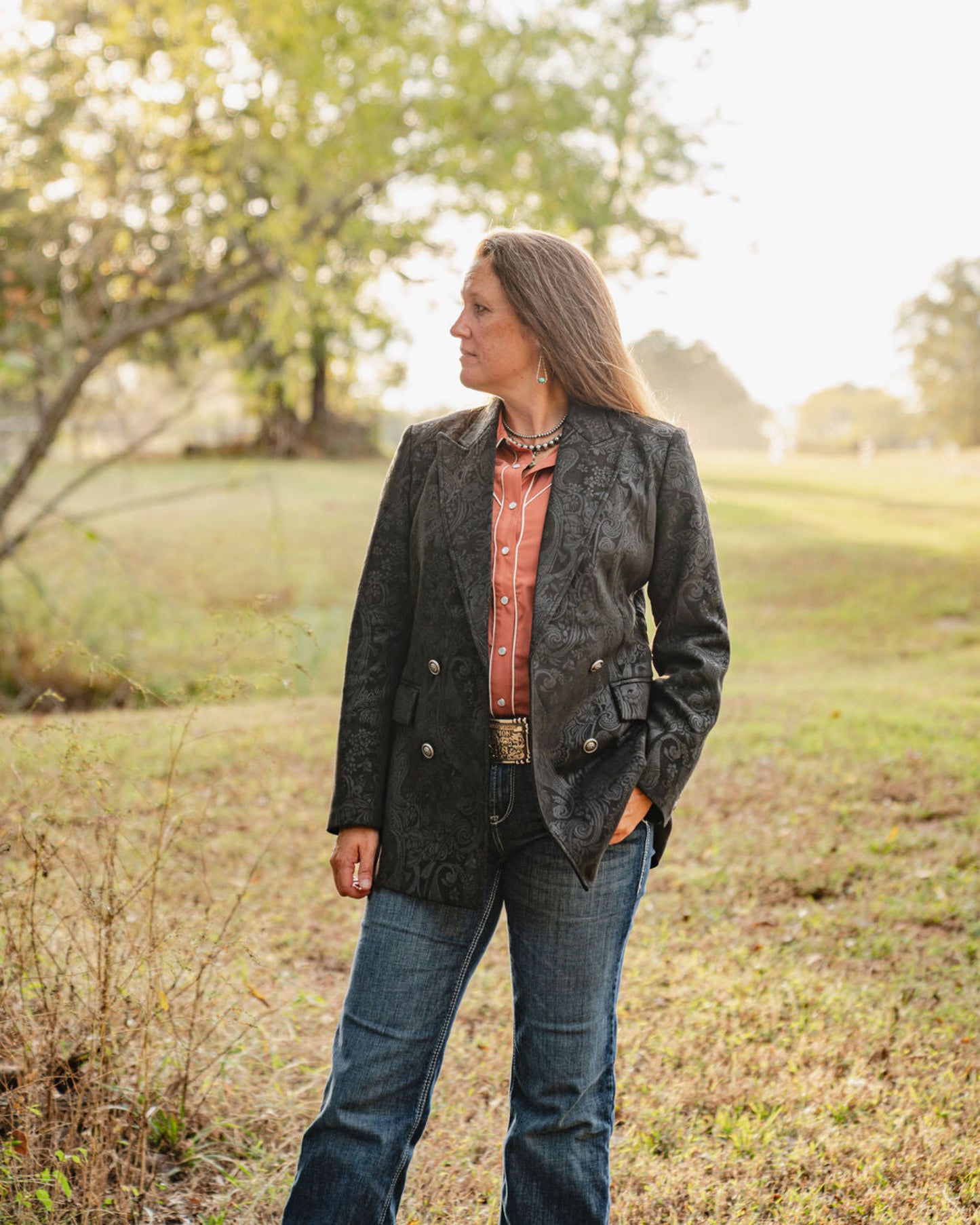 Woman standing in a field wearing a dark jacket and jeans.