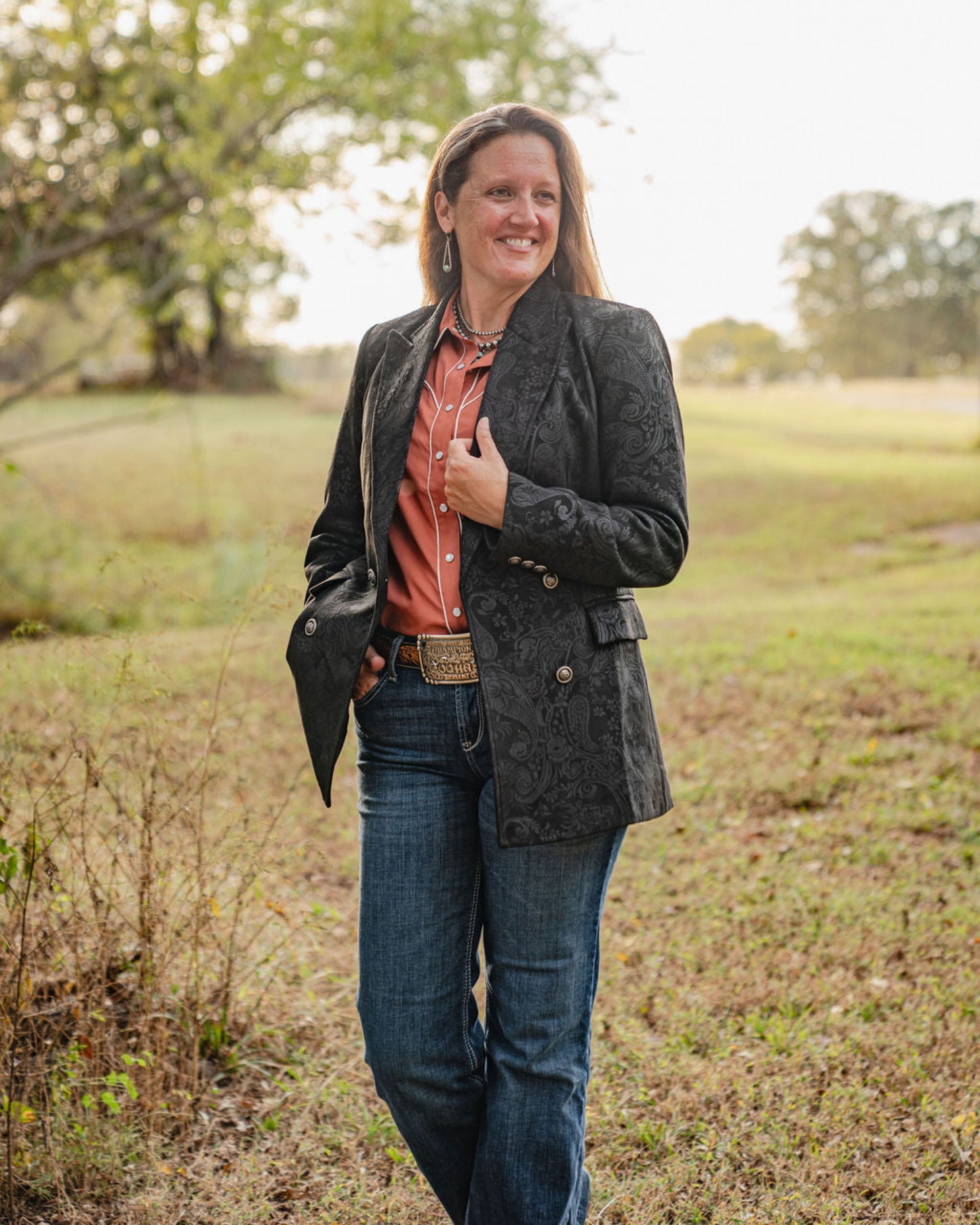 Woman standing in a field wearing a dark jacket and jeans.