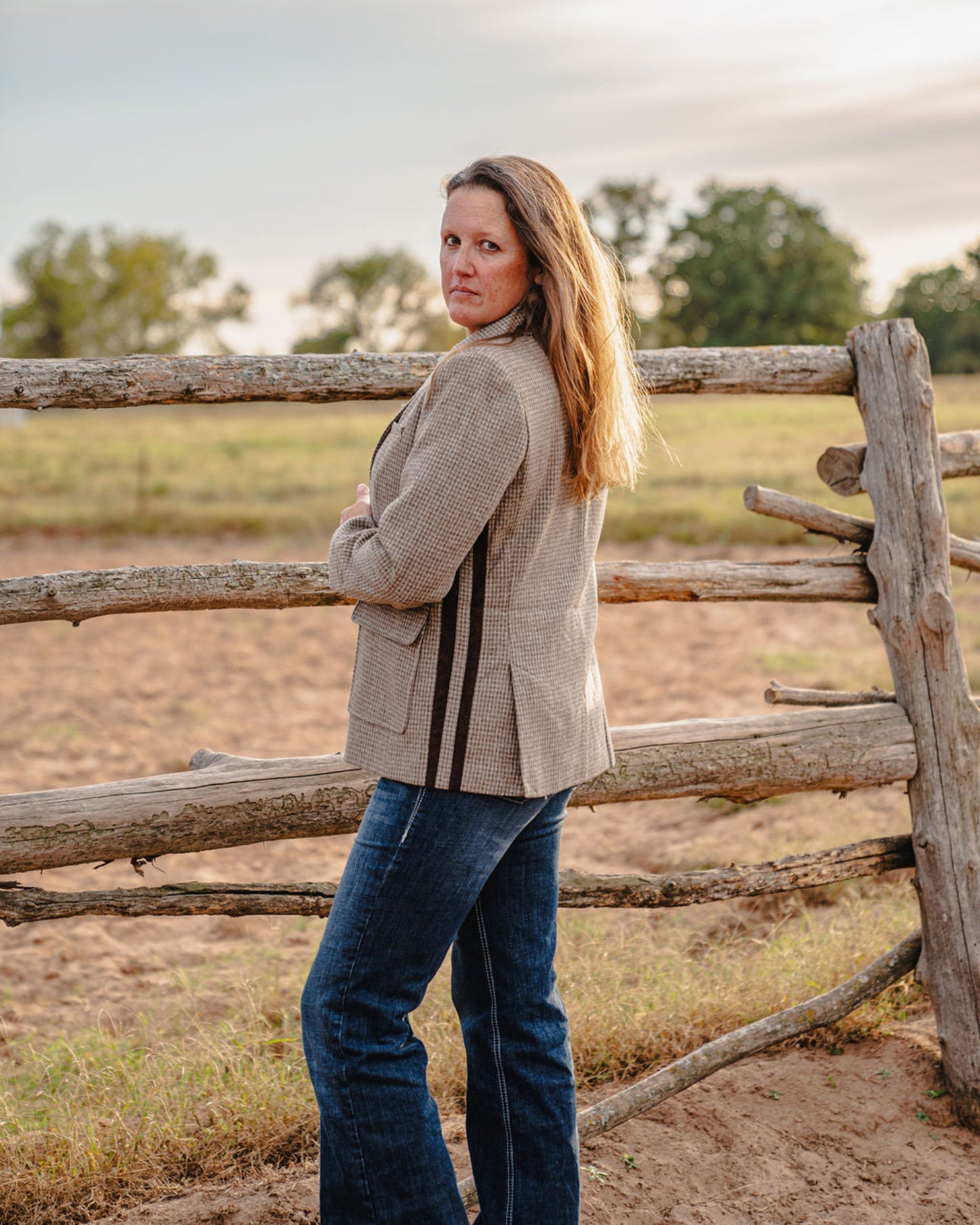 Woman standing by a wooden fence in a rural setting