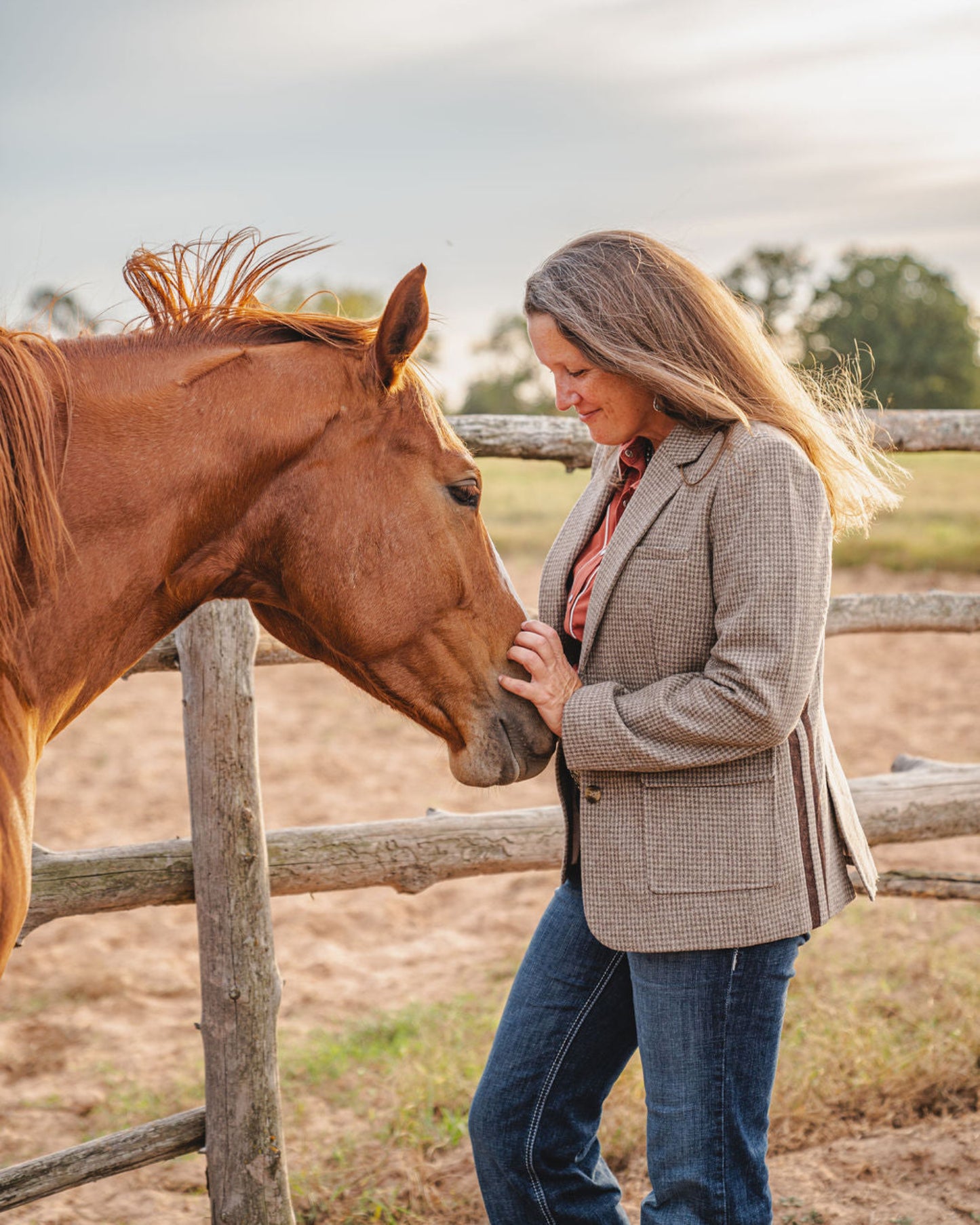 Woman standing next to a horse near a wooden fence with a natural background