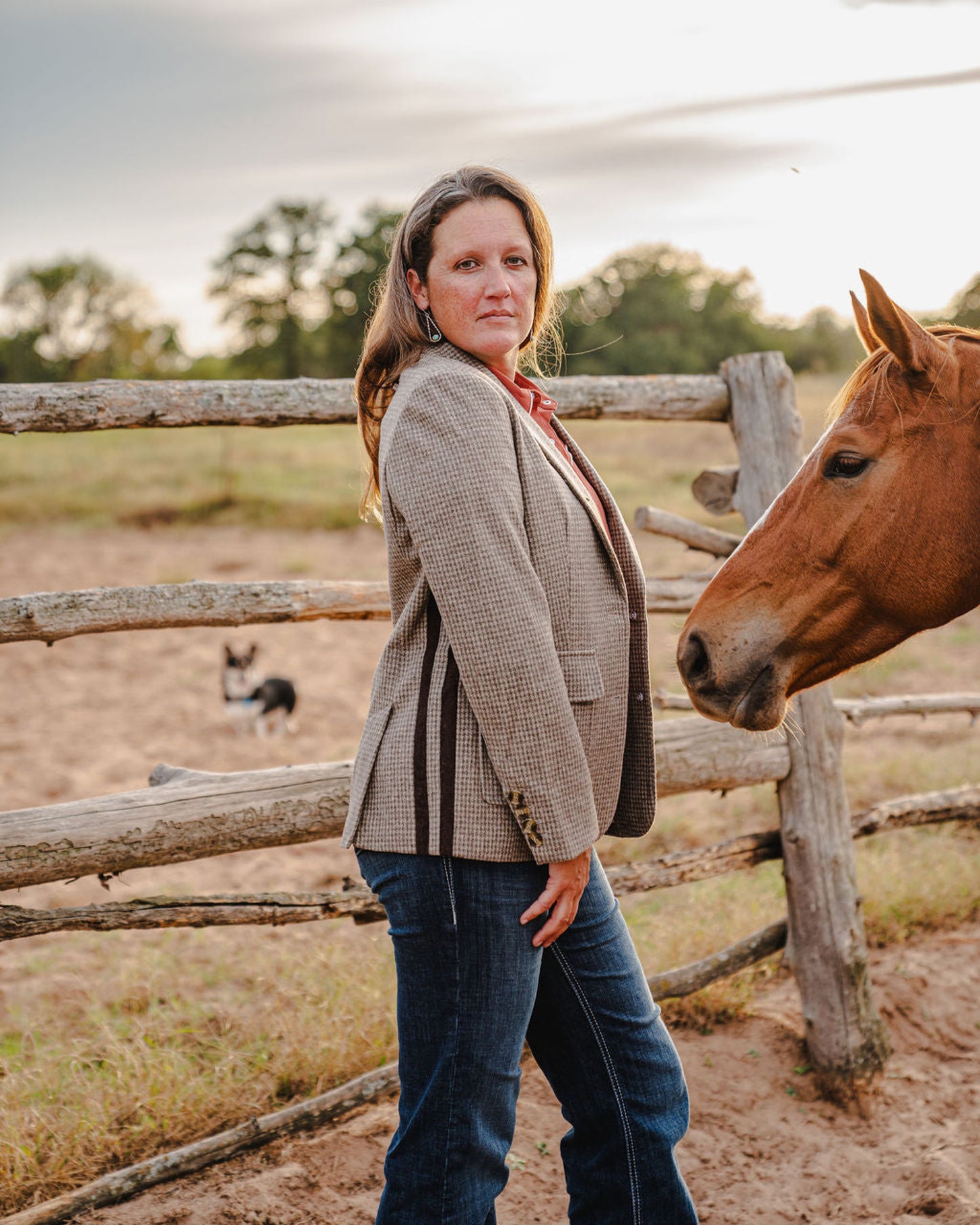 Woman standing next to a horse in an outdoor setting with a wooden fence and open field.