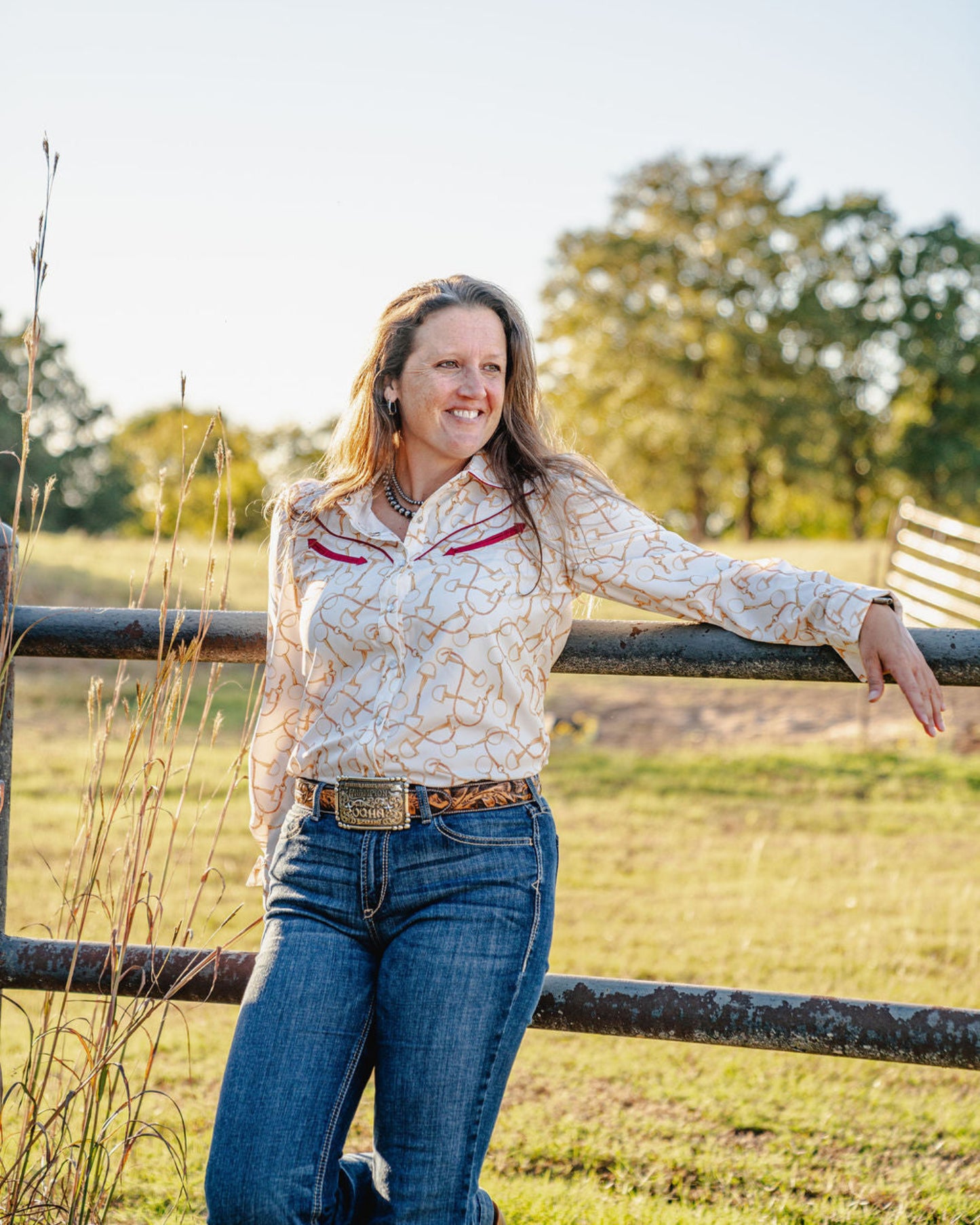 woman standing in front of a fence wearing a long sleeved shirt and jeans
