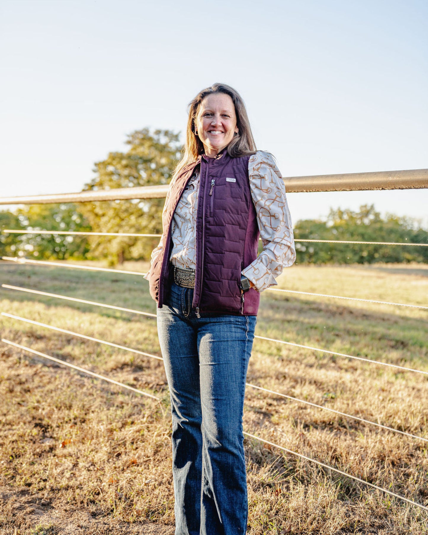 Woman standing in a field wearing a purple vest and jeans.