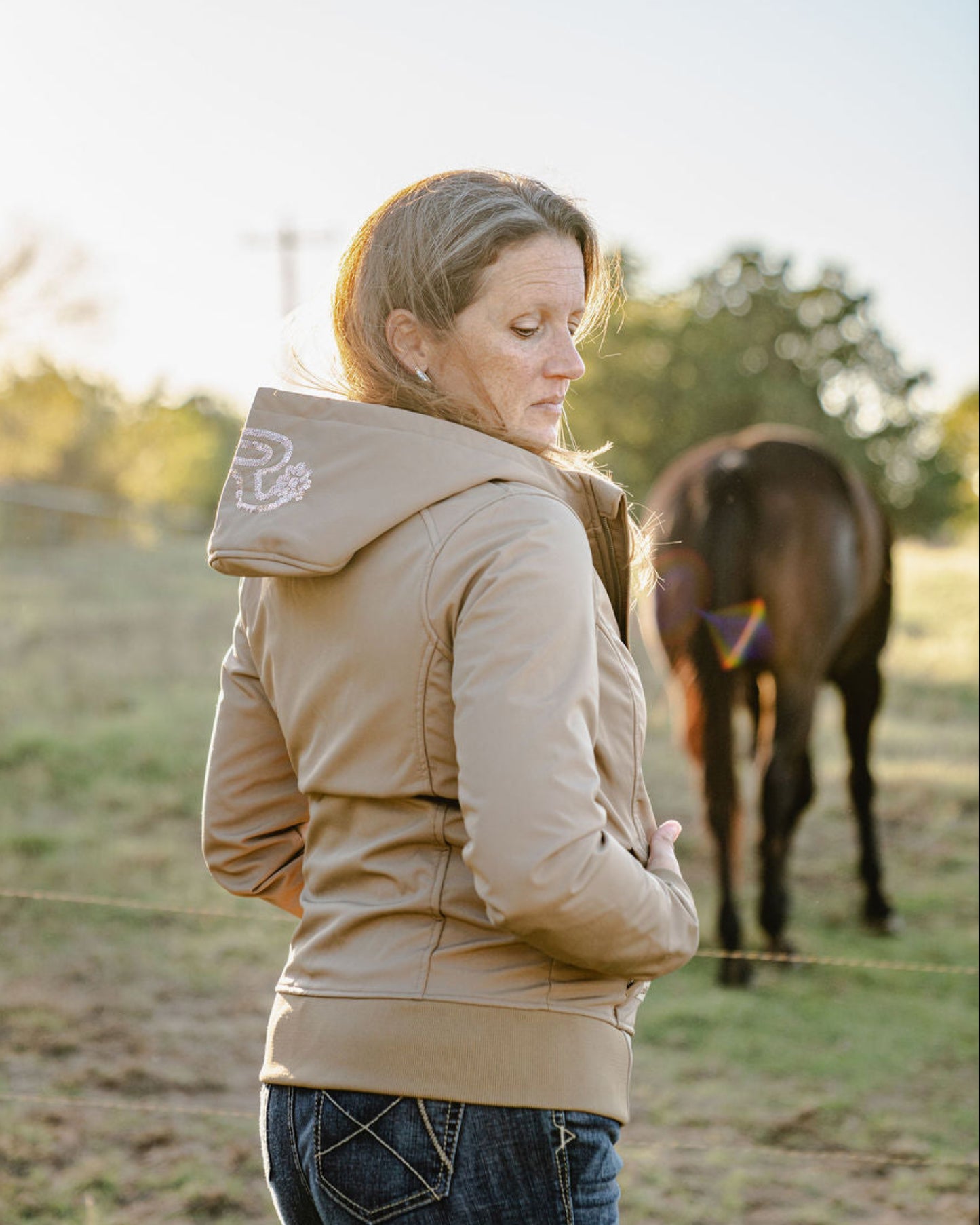 Woman in a beige jacket standing next to a horse in an outdoor setting