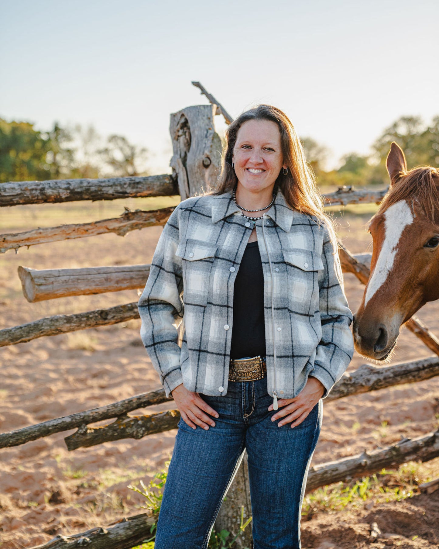 Woman standing next to a horse near a wooden fence in a rural setting