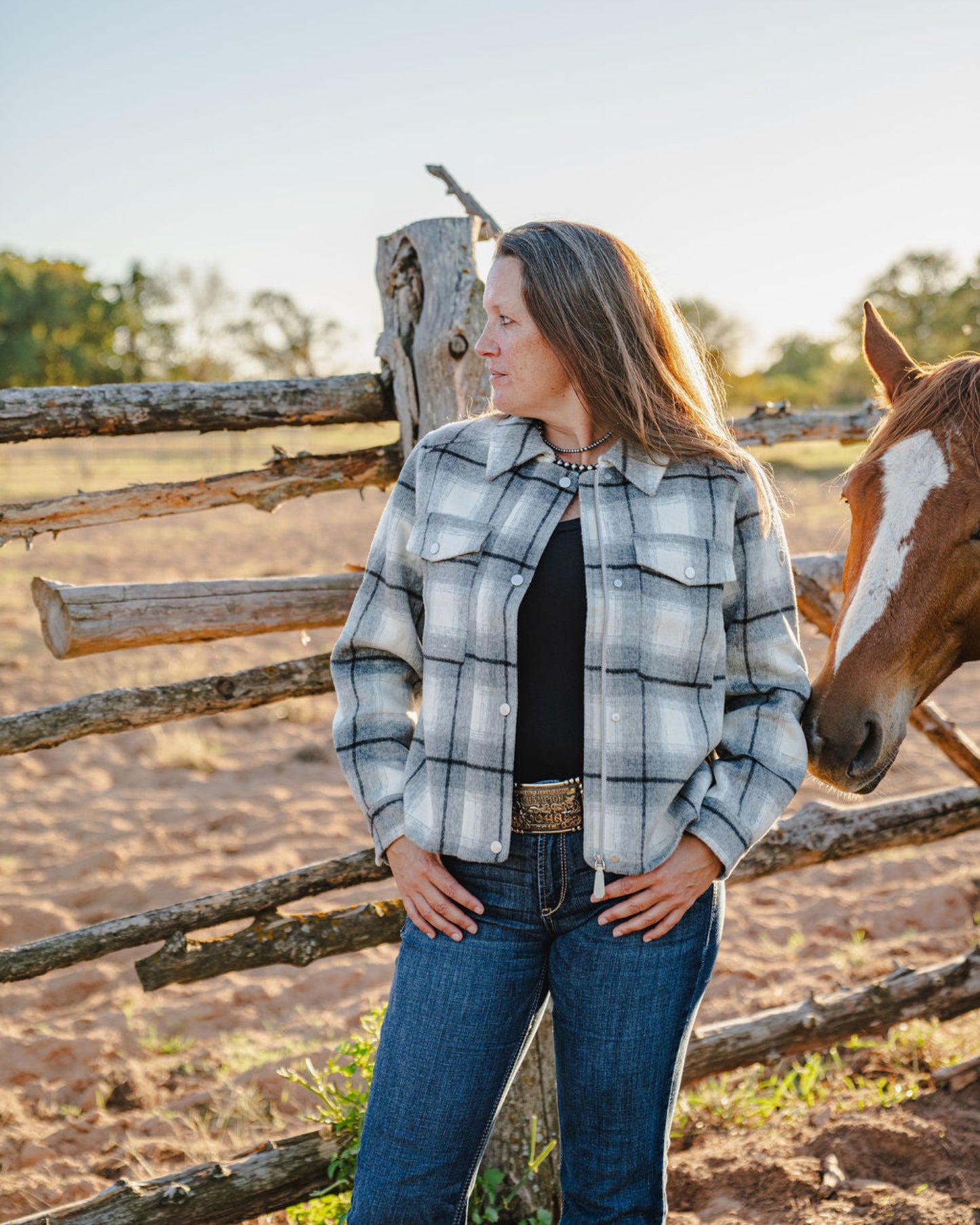 Woman standing next to a horse near a wooden fence in a rural setting