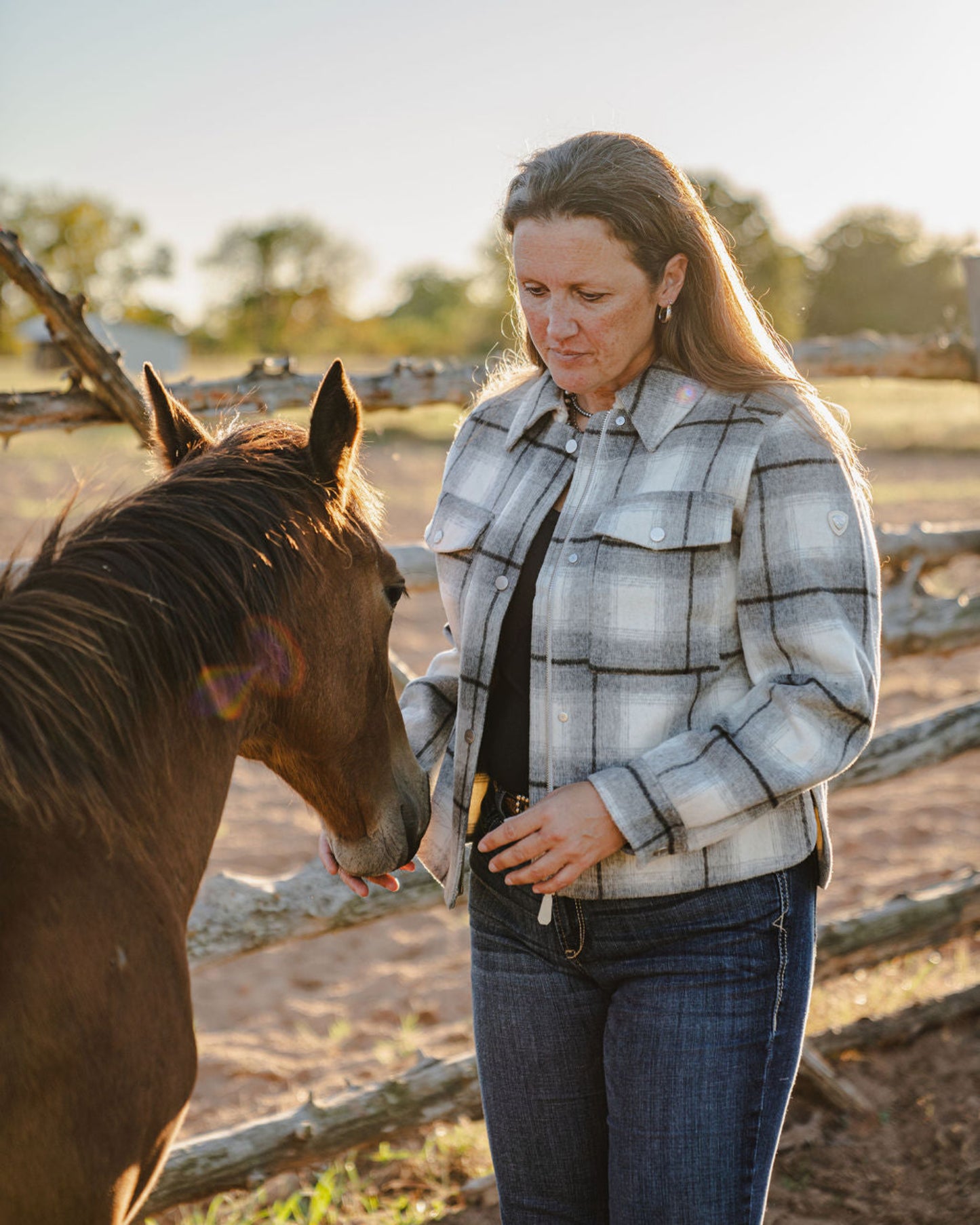 Woman in a plaid jacket standing next to a horse in an outdoor setting