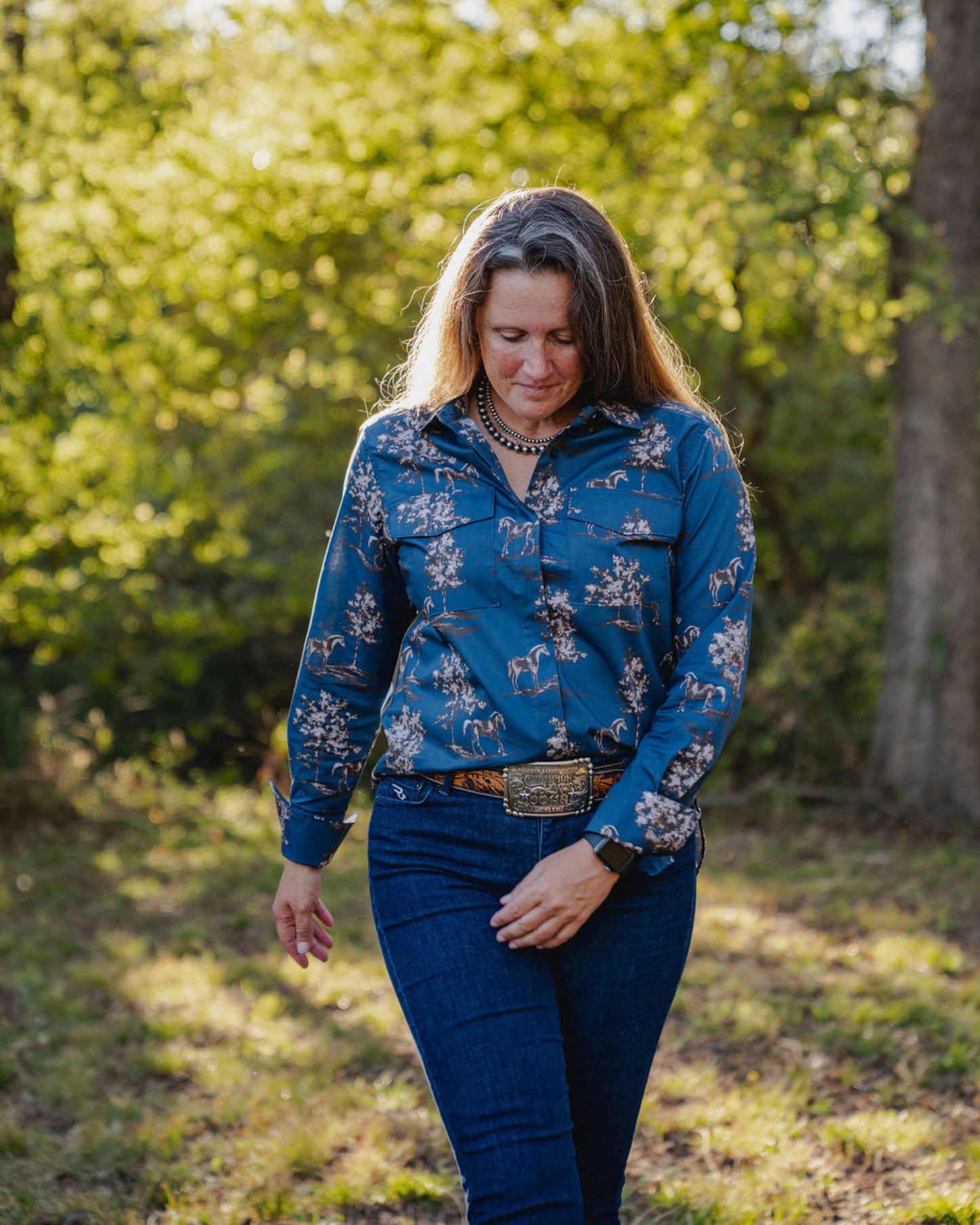 Woman wearing a blue floral shirt and jeans standing in a forested area