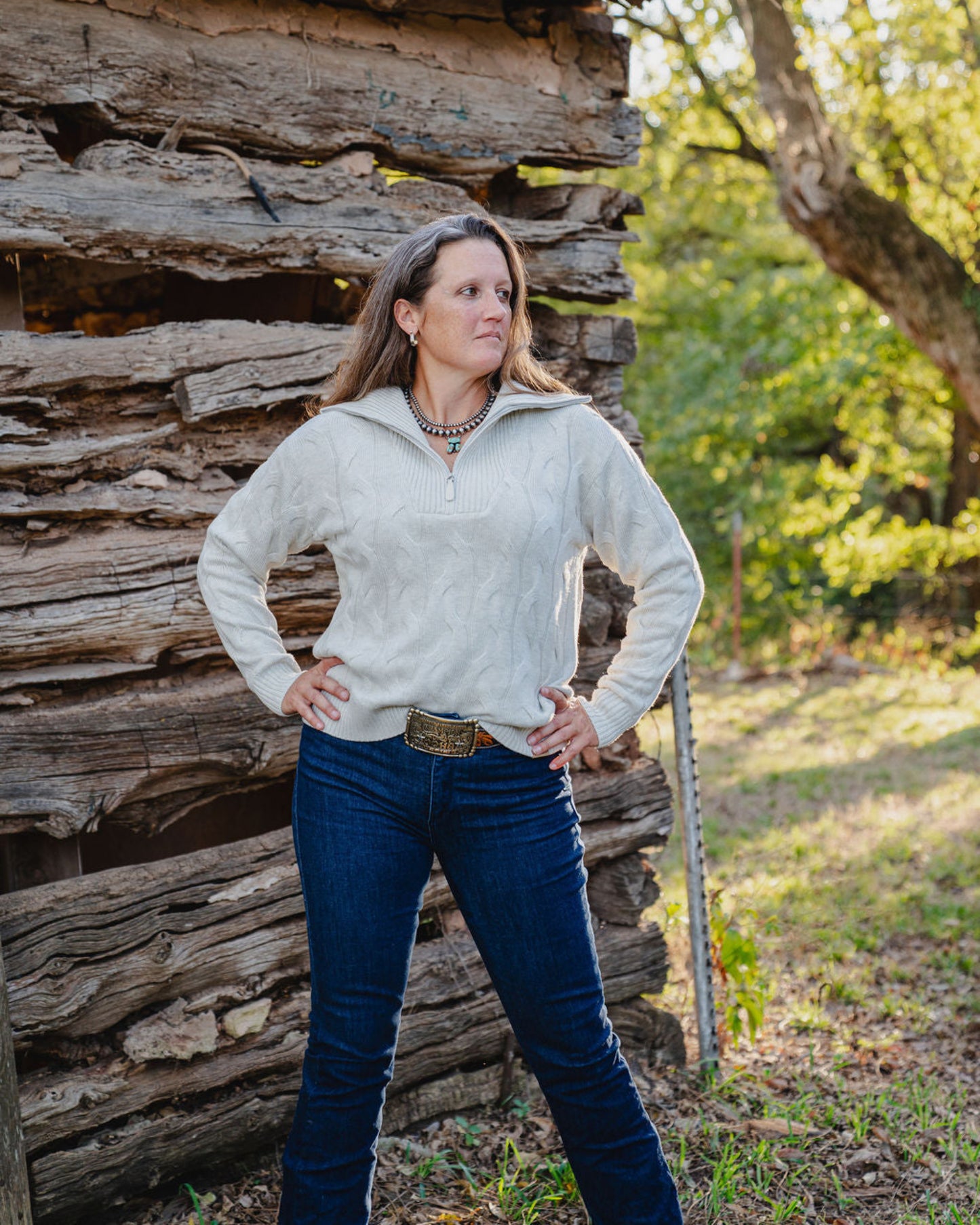 Woman standing in front of a rustic wooden building with trees in the background