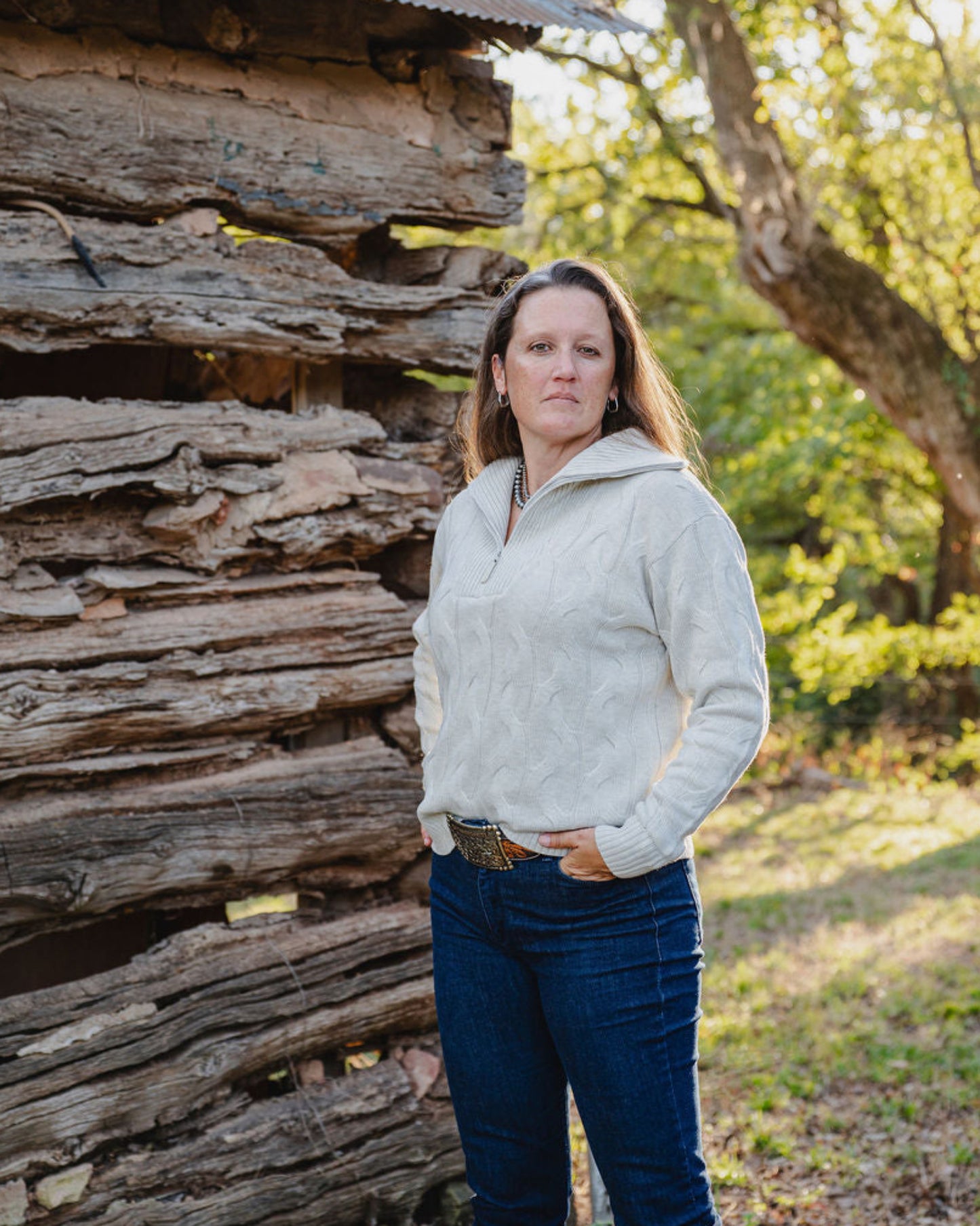 Woman standing in front of a rustic wooden cabin with trees in the background