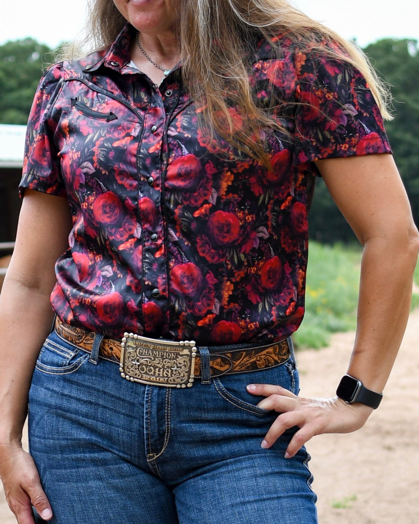Person wearing a colorful floral shirt and blue jeans with a belt, outdoors.