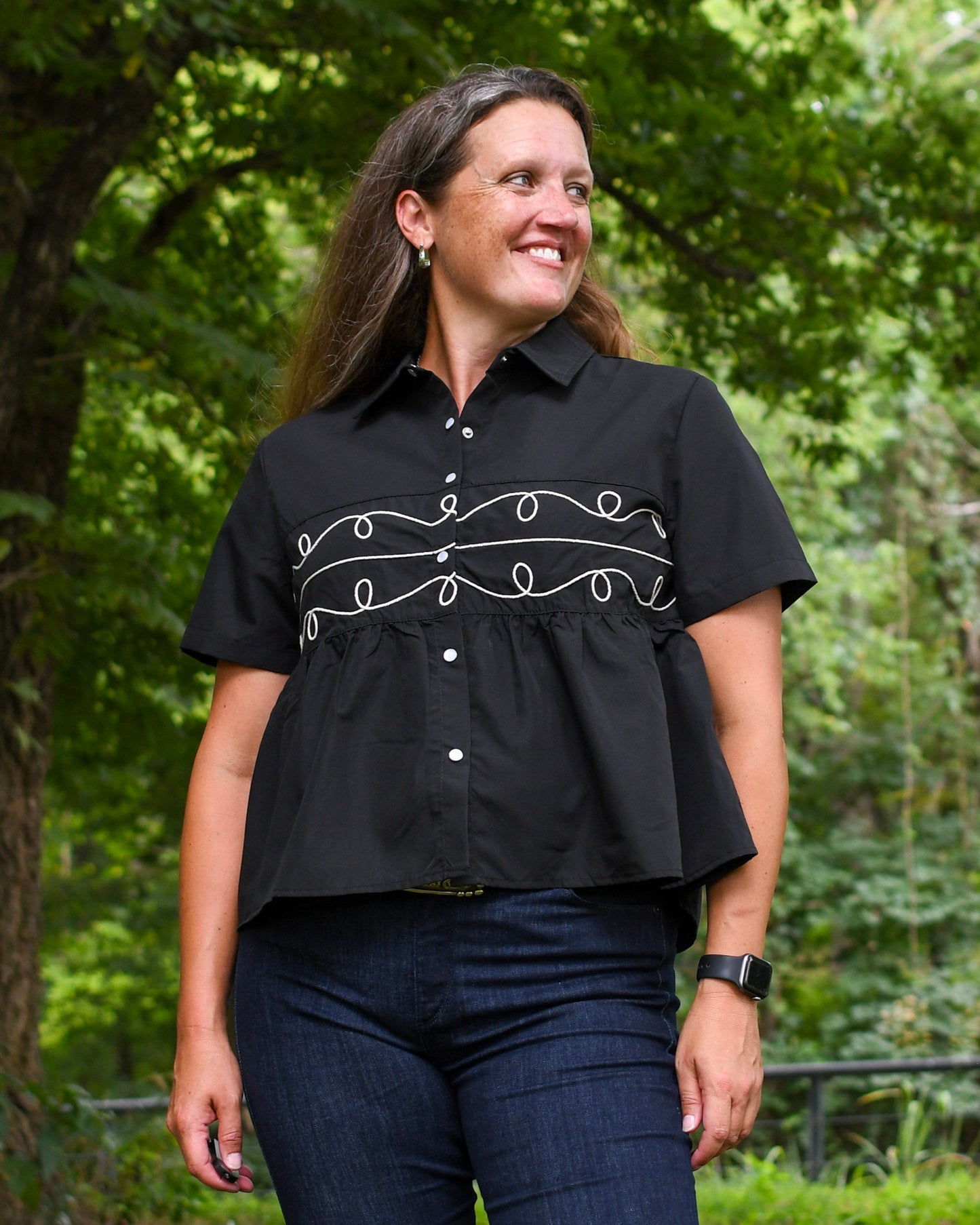 Woman wearing a black blouse with white embroidery in a forest setting