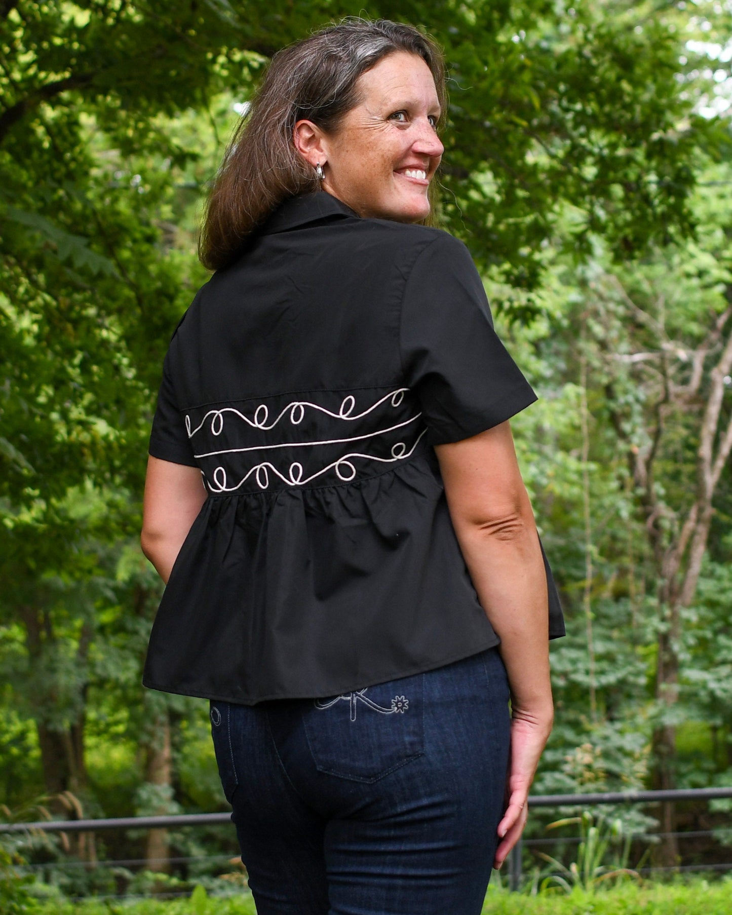 Woman wearing a black blouse with white embroidery in a forest setting