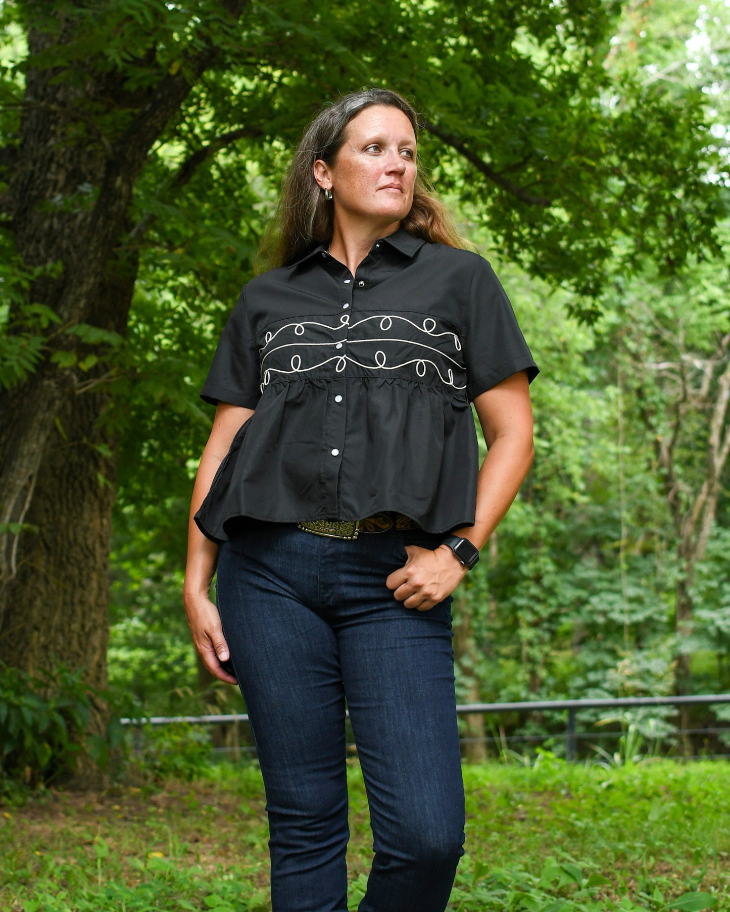 Woman wearing a black blouse with white embroidery in a forest setting