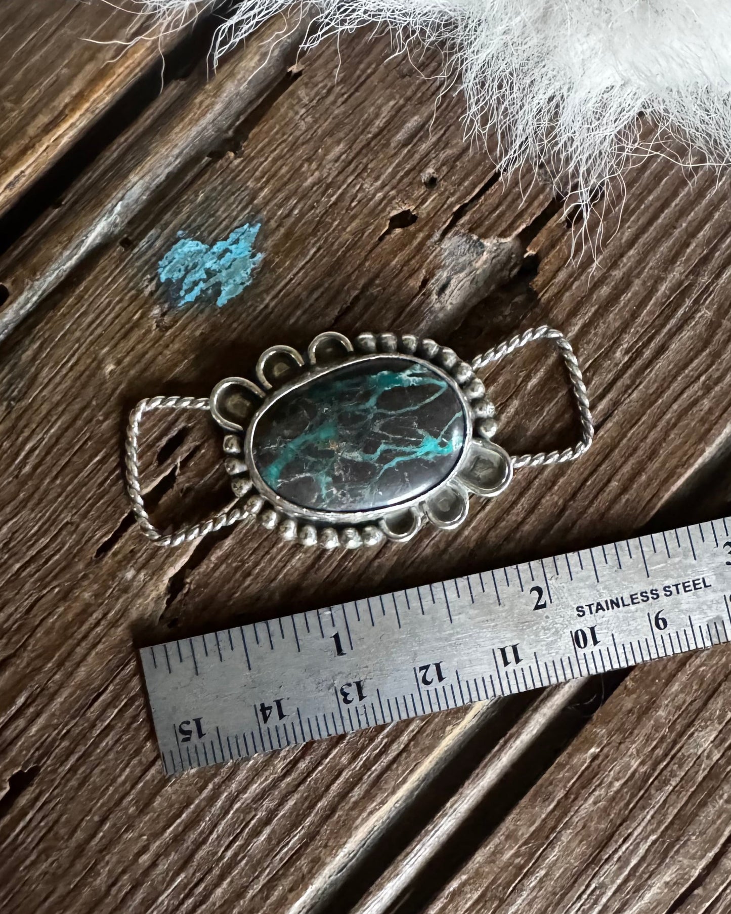 Silver pendant with a turquoise stone on a wooden surface with a ruler for scale.