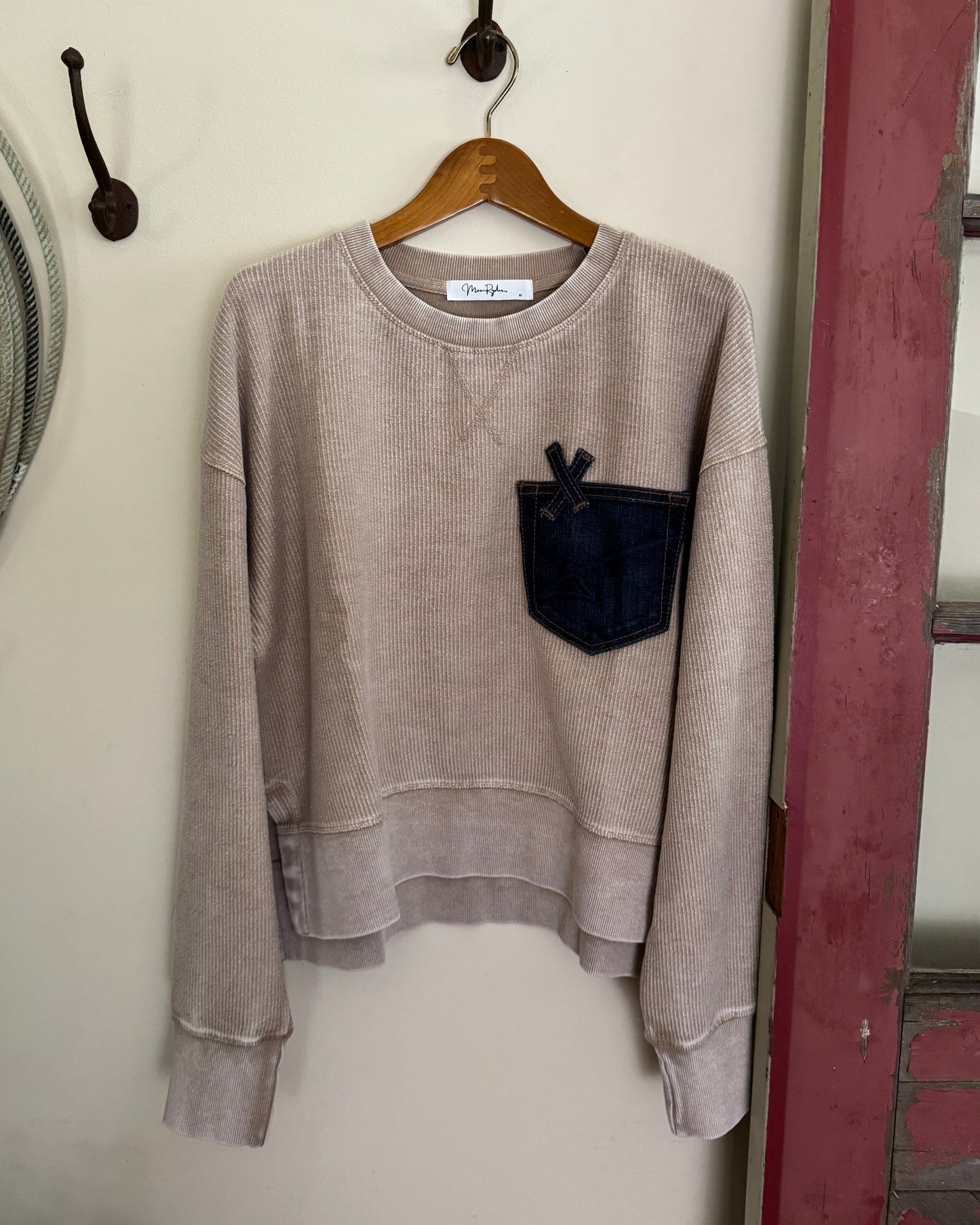 Folded beige sweater on a wooden hanger against a white wall.
