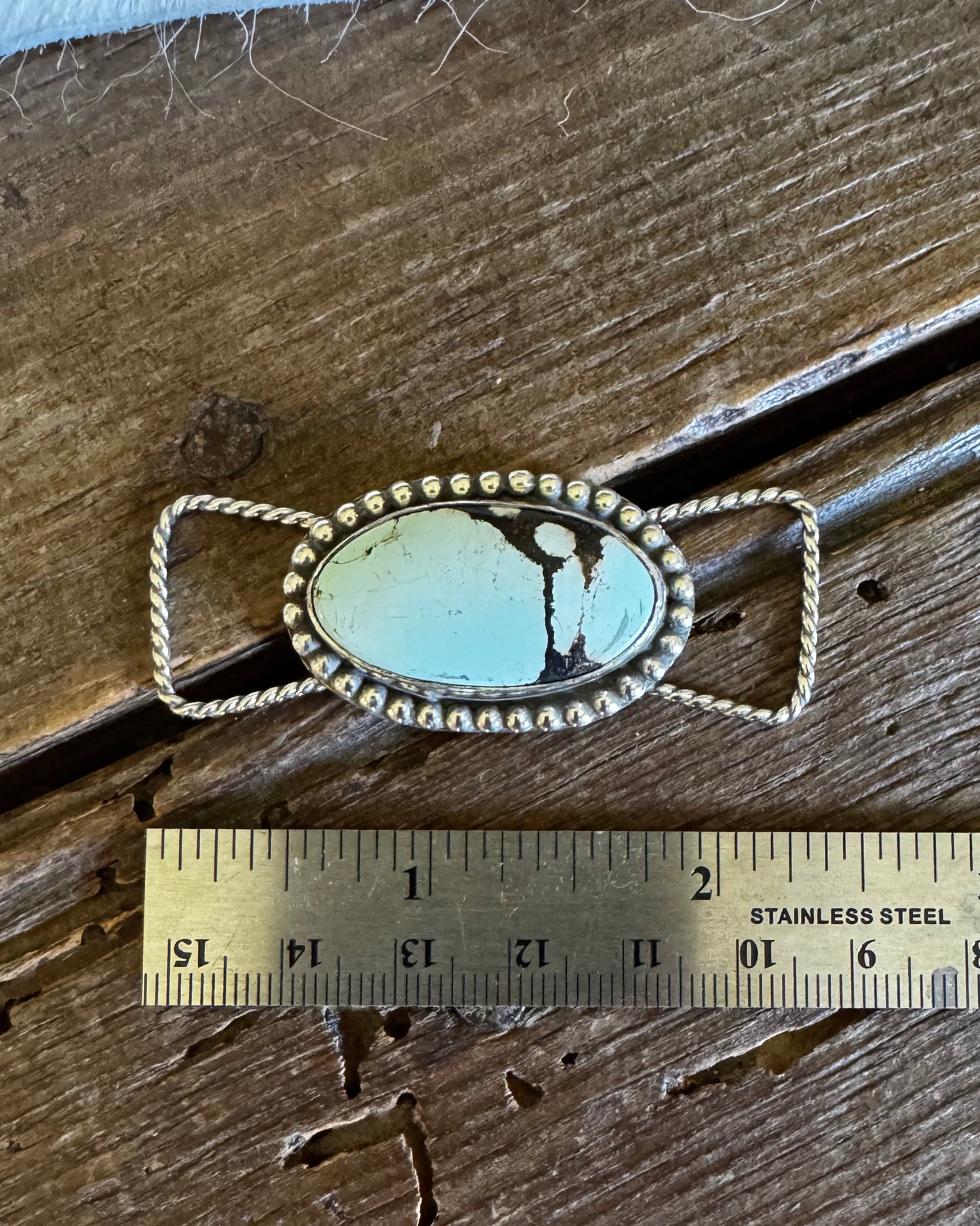 Silver twilly slide with turquoise stone next to a ruler on a wooden surface