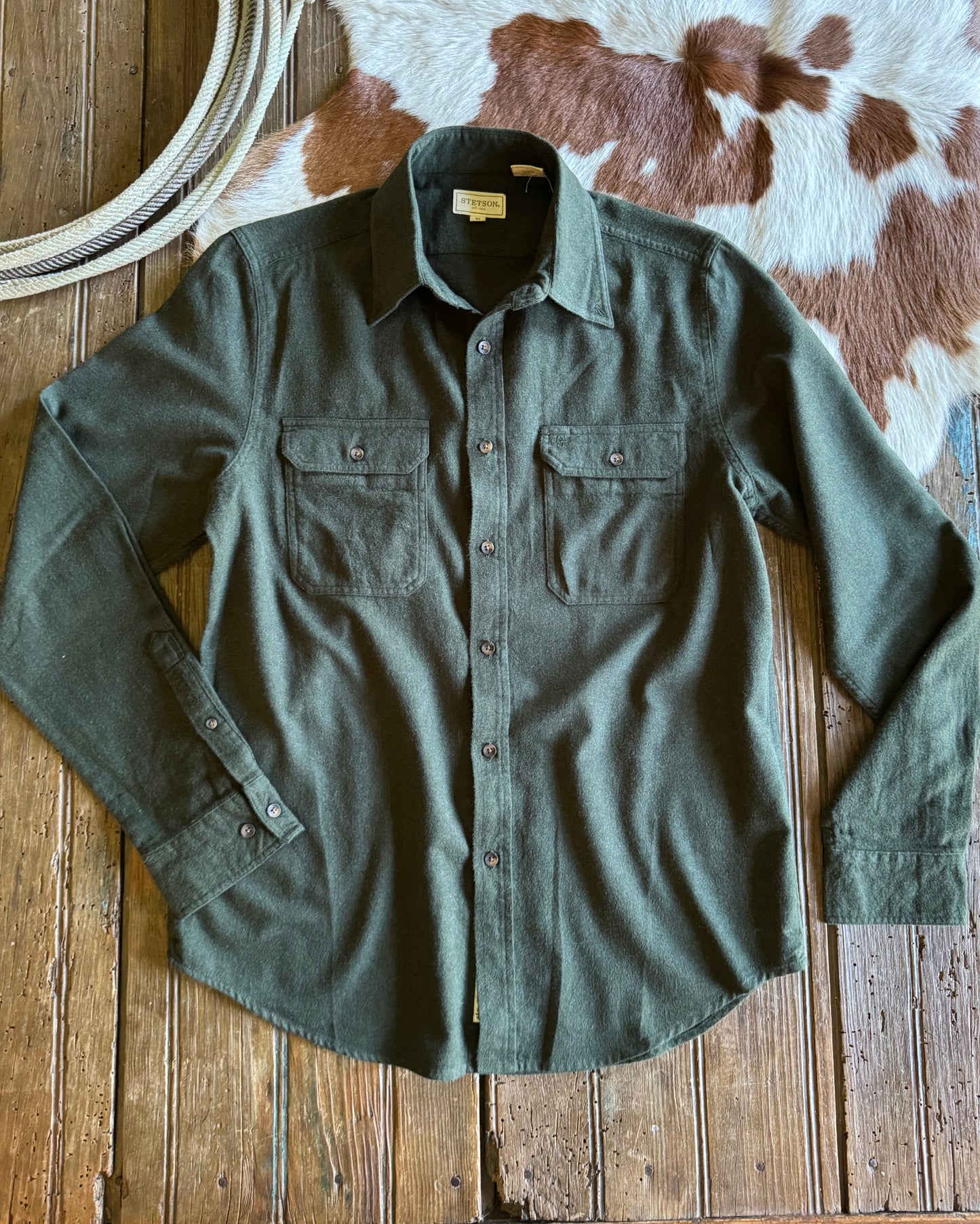 Green shirt on a wooden surface with a cowhide rug and rope in the background