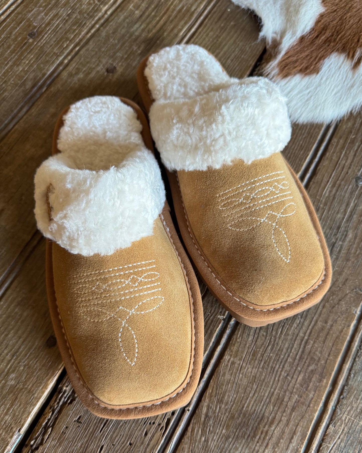 Pair of tan slippers with white fur lining on a wooden floor.