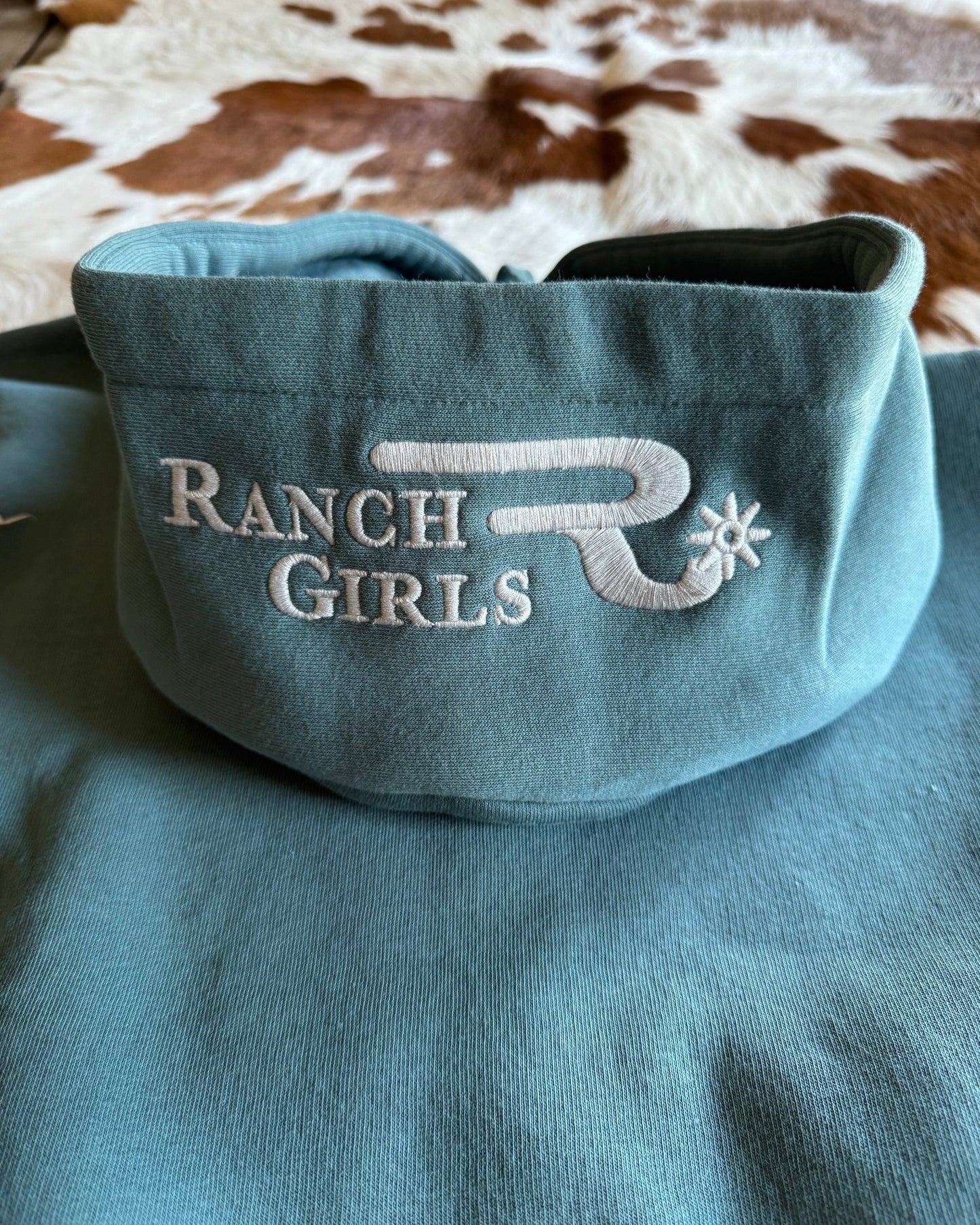 Blue hoodie with 'Ranch Girls' logo on a blurred background