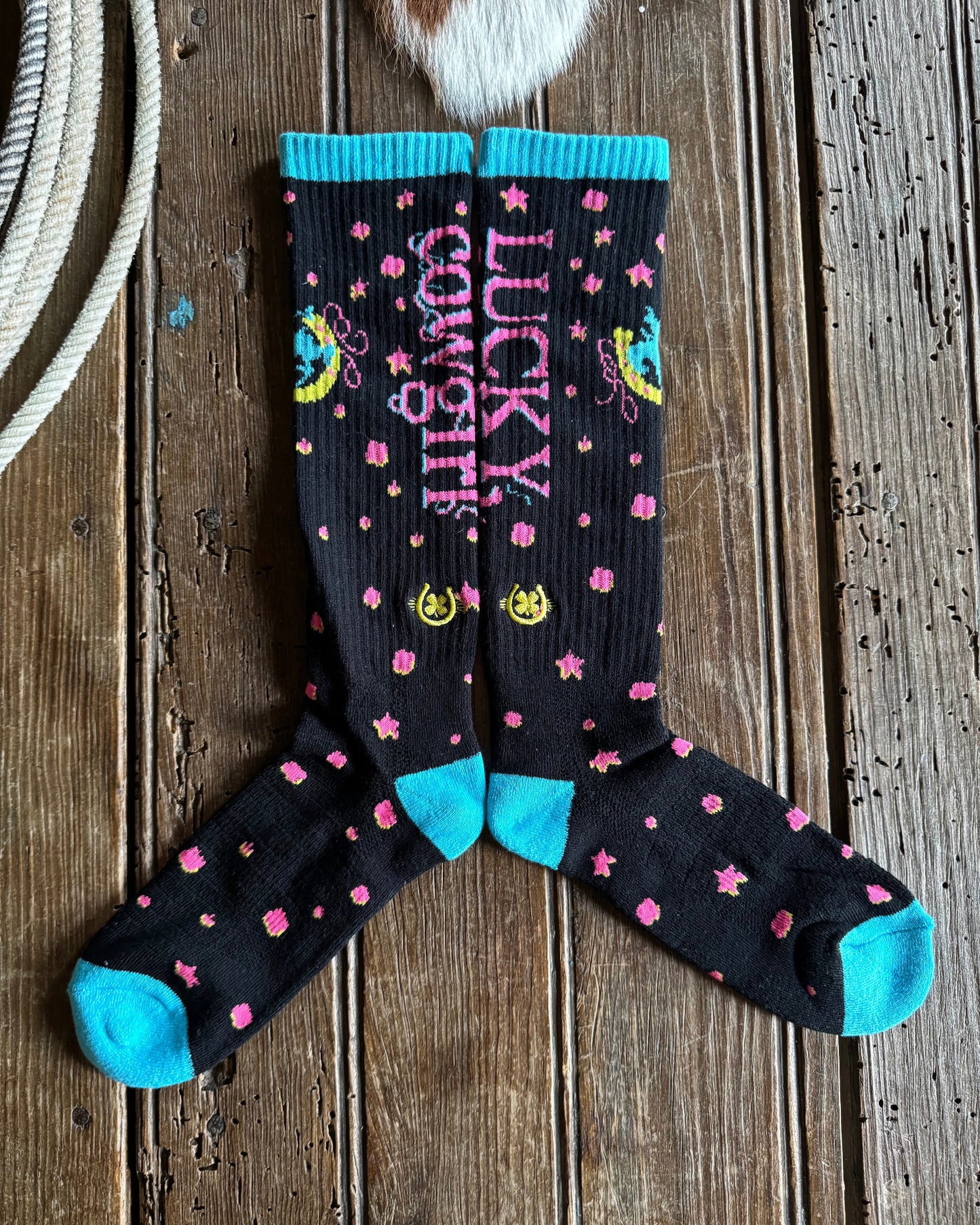 Pair of socks with 'Lucky Cowgirl' text on a wooden surface