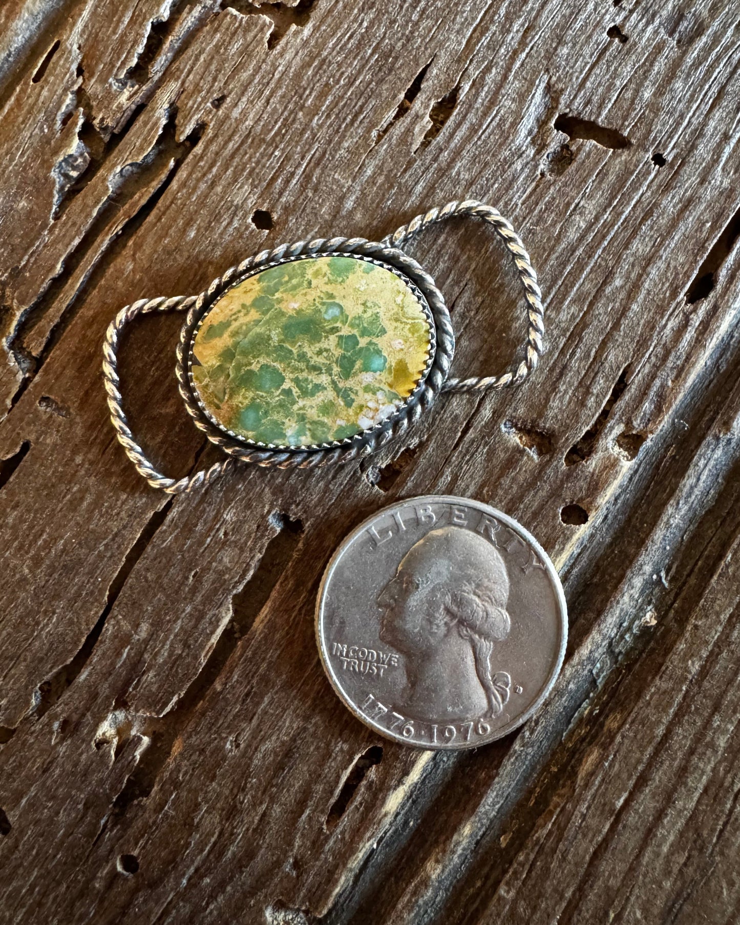 Ring with a green stone next to a penny on a wooden surface